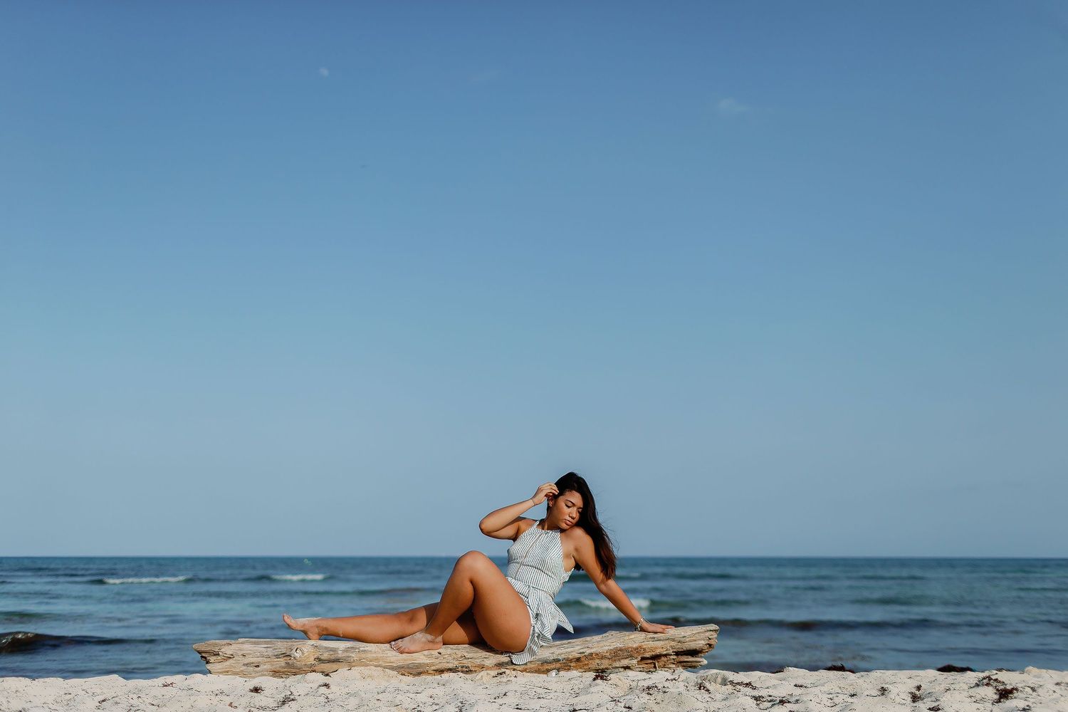 Senior portrait session in Los Cabos featuring a young woman posing on driftwood along a scenic beach with ocean views.