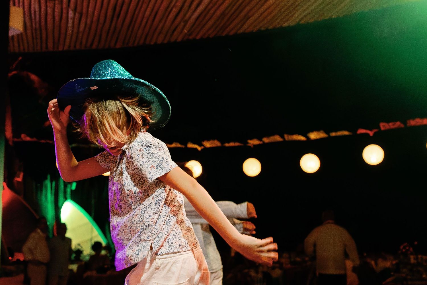 A young wedding guest dances in a sparkling party hat at the reception.