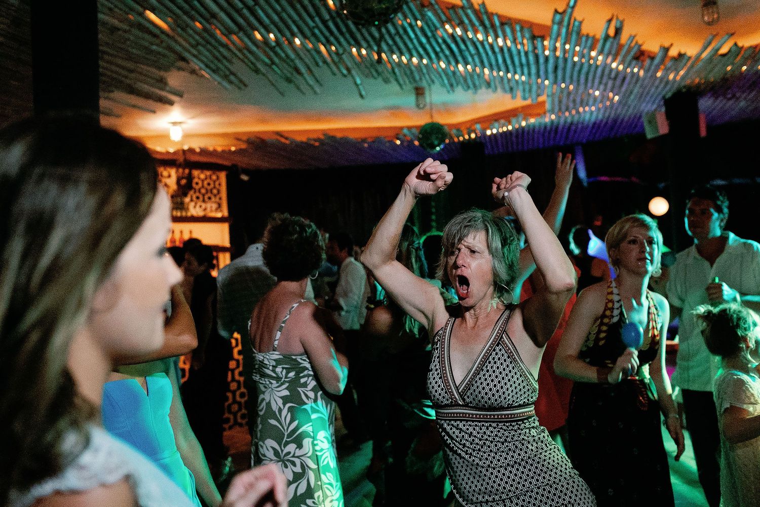 An enthusiastic guest celebrates with her arms raised on the wedding dance floor.