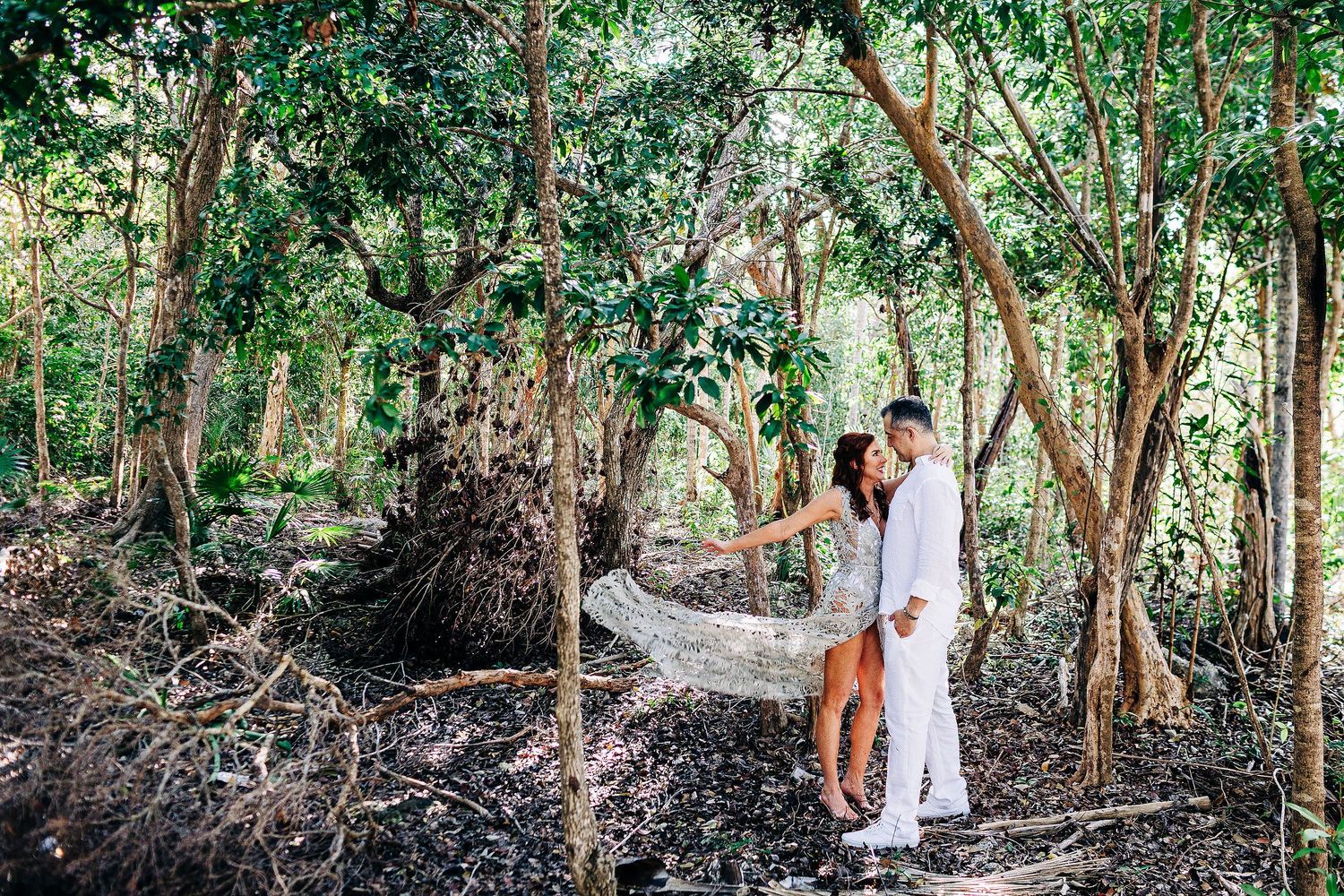 Sarah and Evish embrace in a sunlit tropical forest in Tulum.