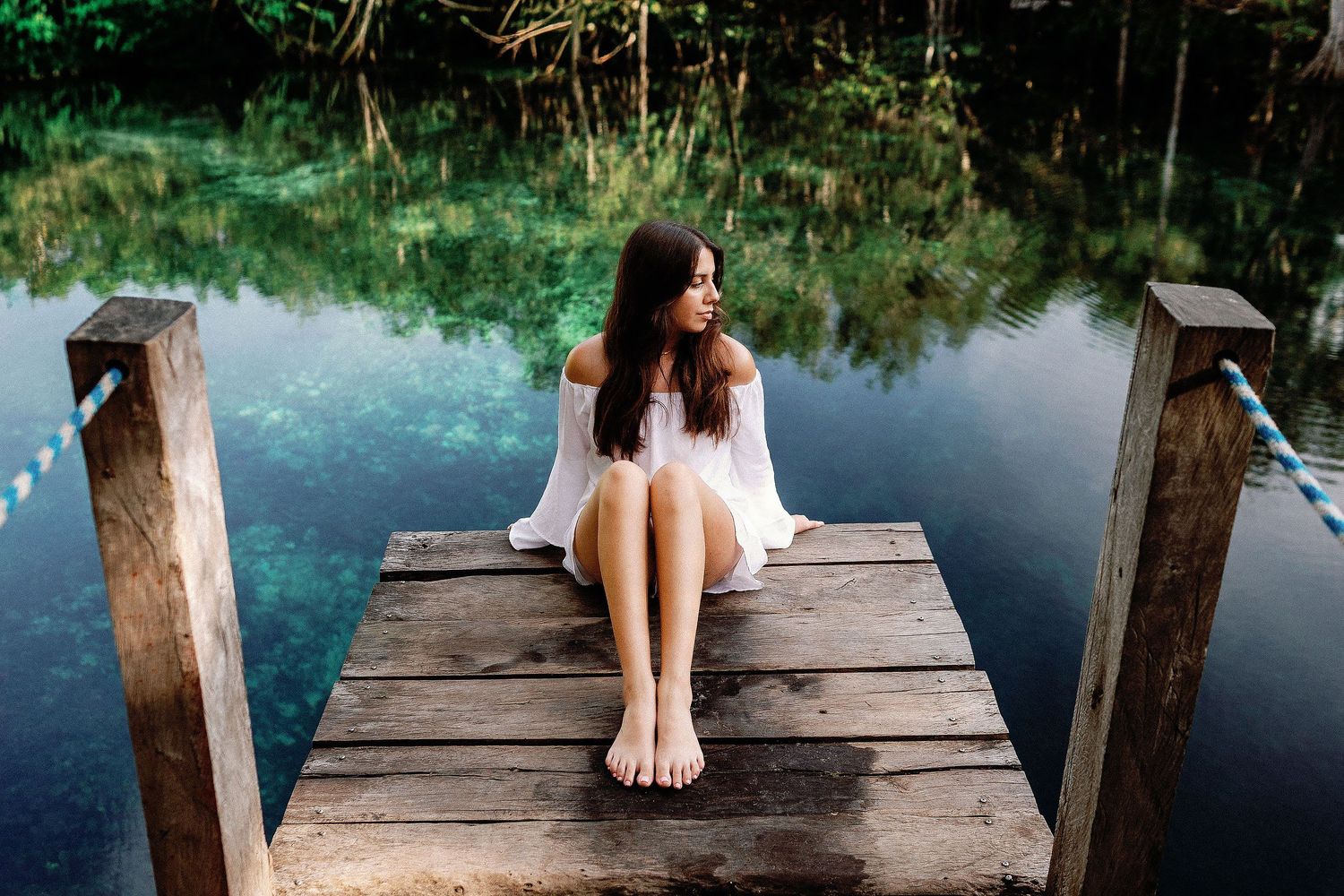 Senior portrait session in Tulum at a crystal-clear cenote featuring a young woman on a wooden dock surrounded by nature.