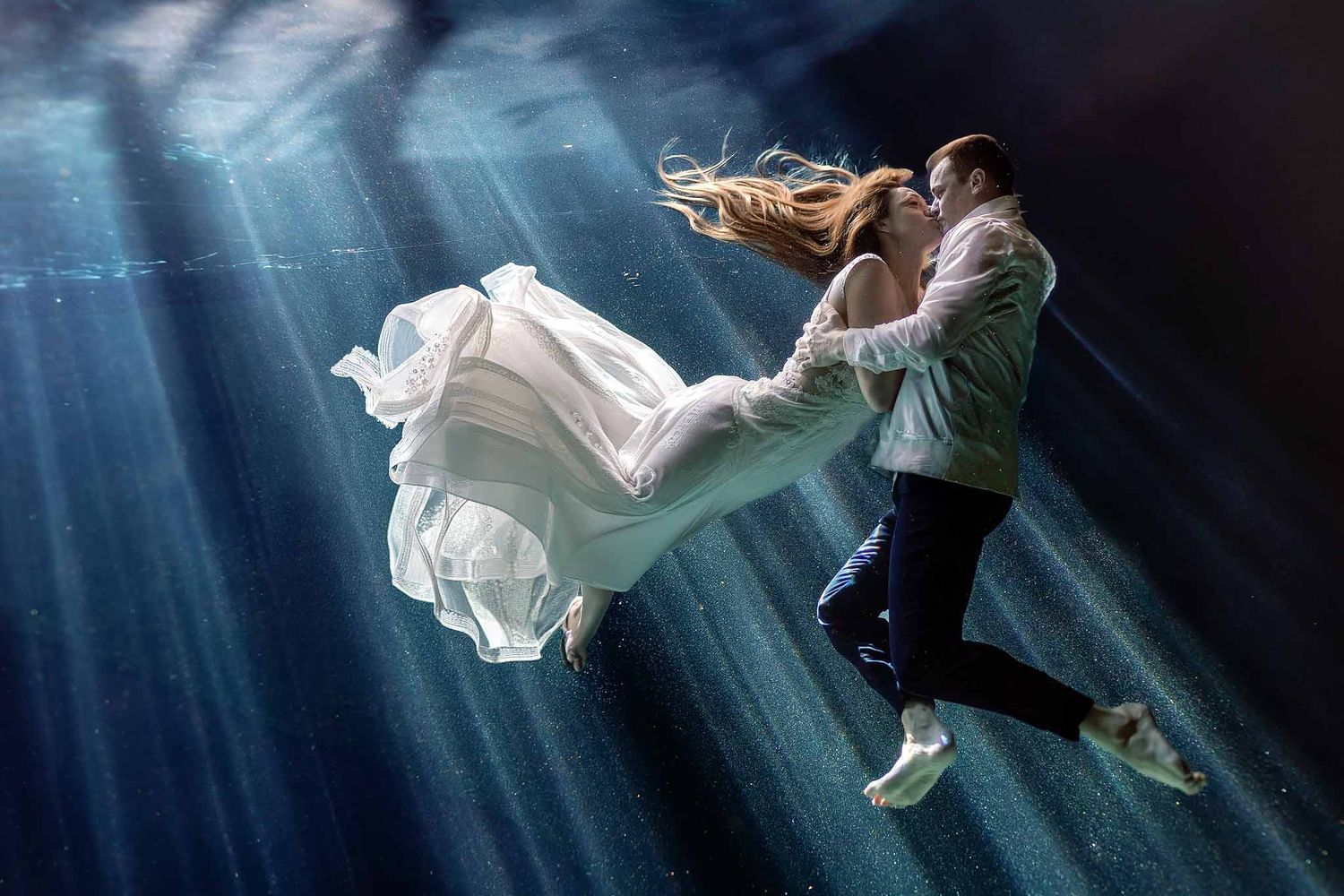 Bride and groom underwater wedding portrait in a Cancun cenote with dramatic light beams and flowing wedding dress.