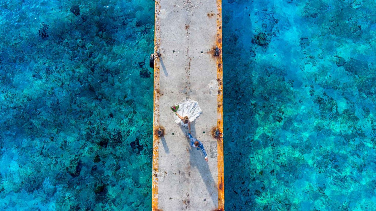 Aerial Isla Mujeres wedding photography of bride and groom on pier surrounded by turquoise Caribbean water