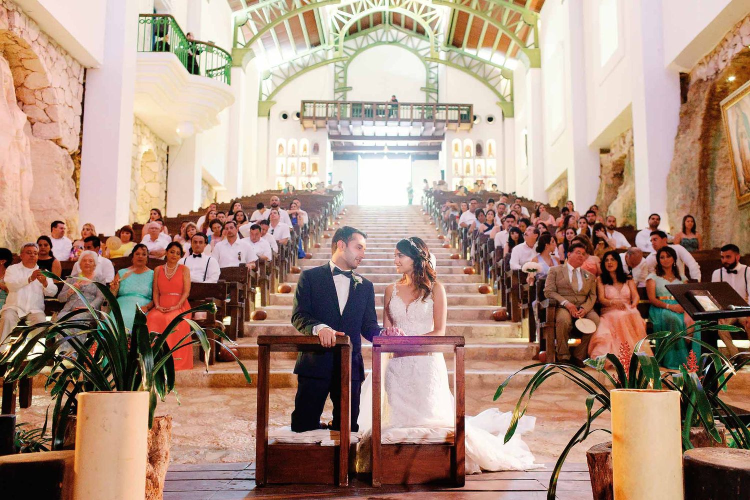 Wedding at Xcaret's Capilla de Guadalupe: Bride and groom at the altar, viewed from the priest's perspective in the tiered stone chapel