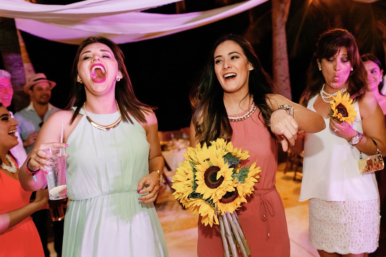 Wedding guests laugh and dance while one woman carries a bright sunflower bouquet.