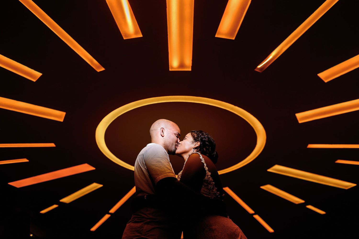 Couple kissing beneath dramatic circular orange ceiling lights during their creative portrait session at Moon Palace Nizuc in Cancun.