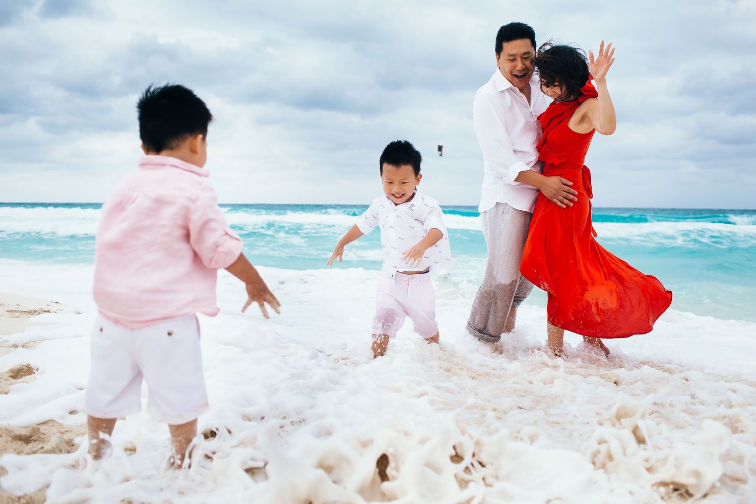 Family wearing elegant tropical beach outfits during a fun family photo session in Cancun Hotel Zone by the Caribbean Sea.