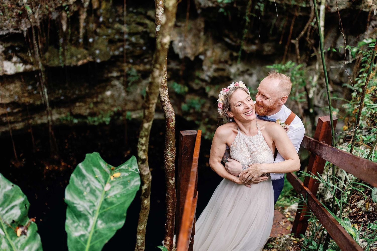 Jeff embraces Veronica as they laugh during their wedding portraits on the wooden stairs at Cenote Hats’uts near Playa del Carmen.