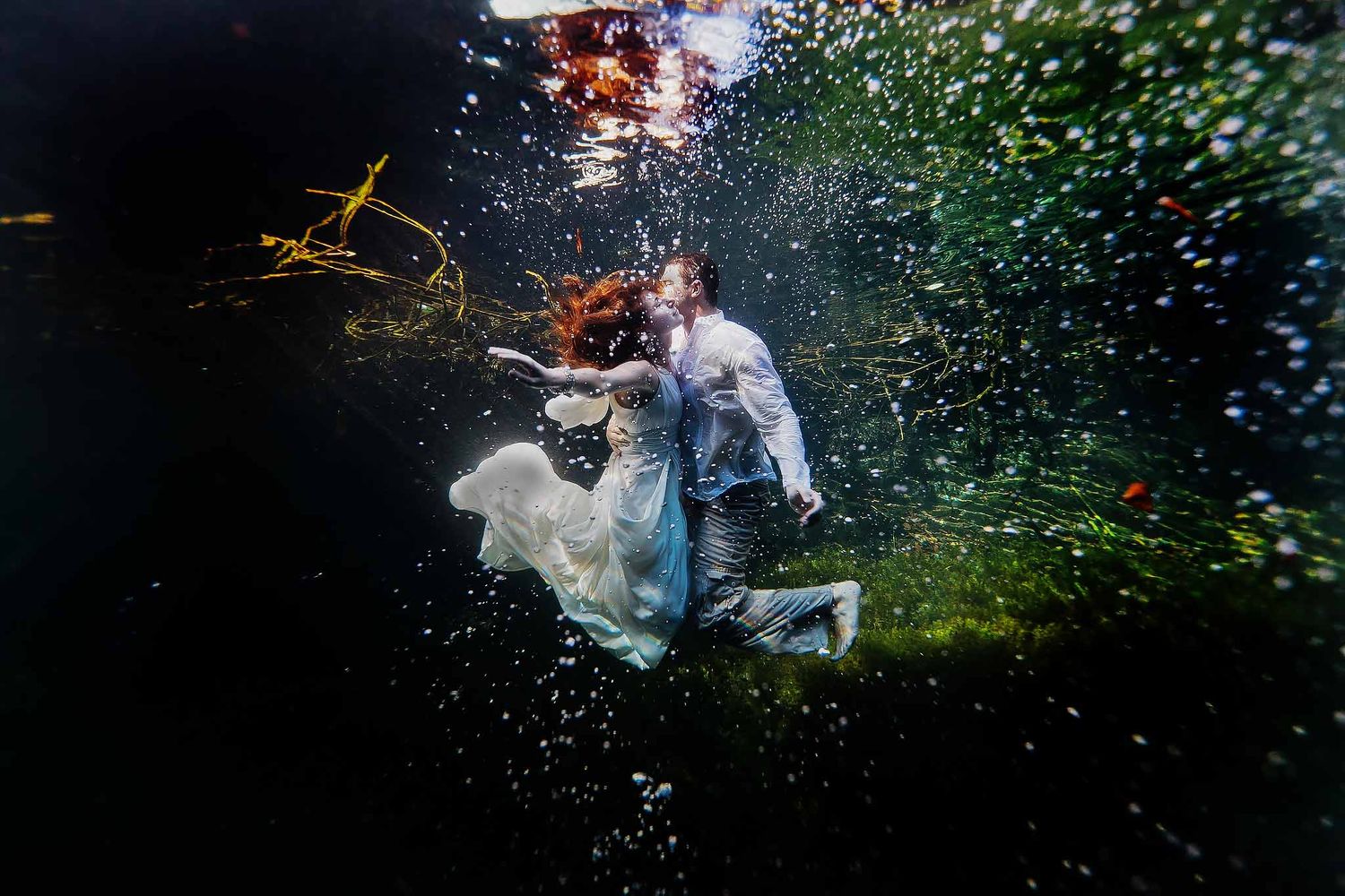 Destination wedding couple underwater in a Riviera Maya cenote captured with cinematic lighting and bubbles.
