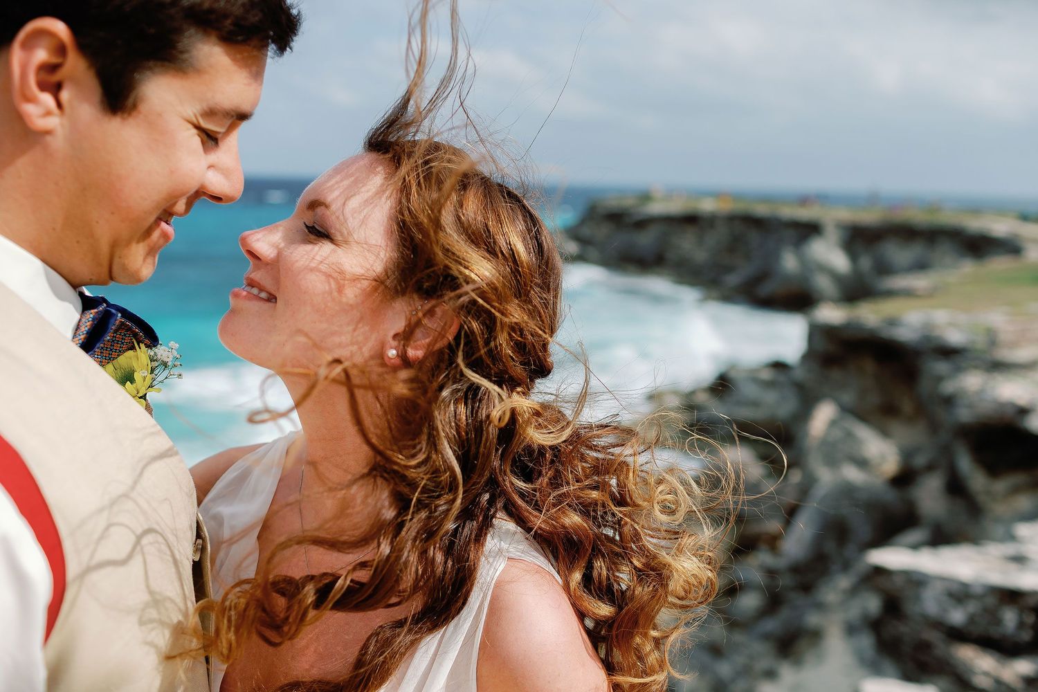Li smiles up at Carlos during a windswept portrait beside Isla Mujeres’s rocky Caribbean coast.