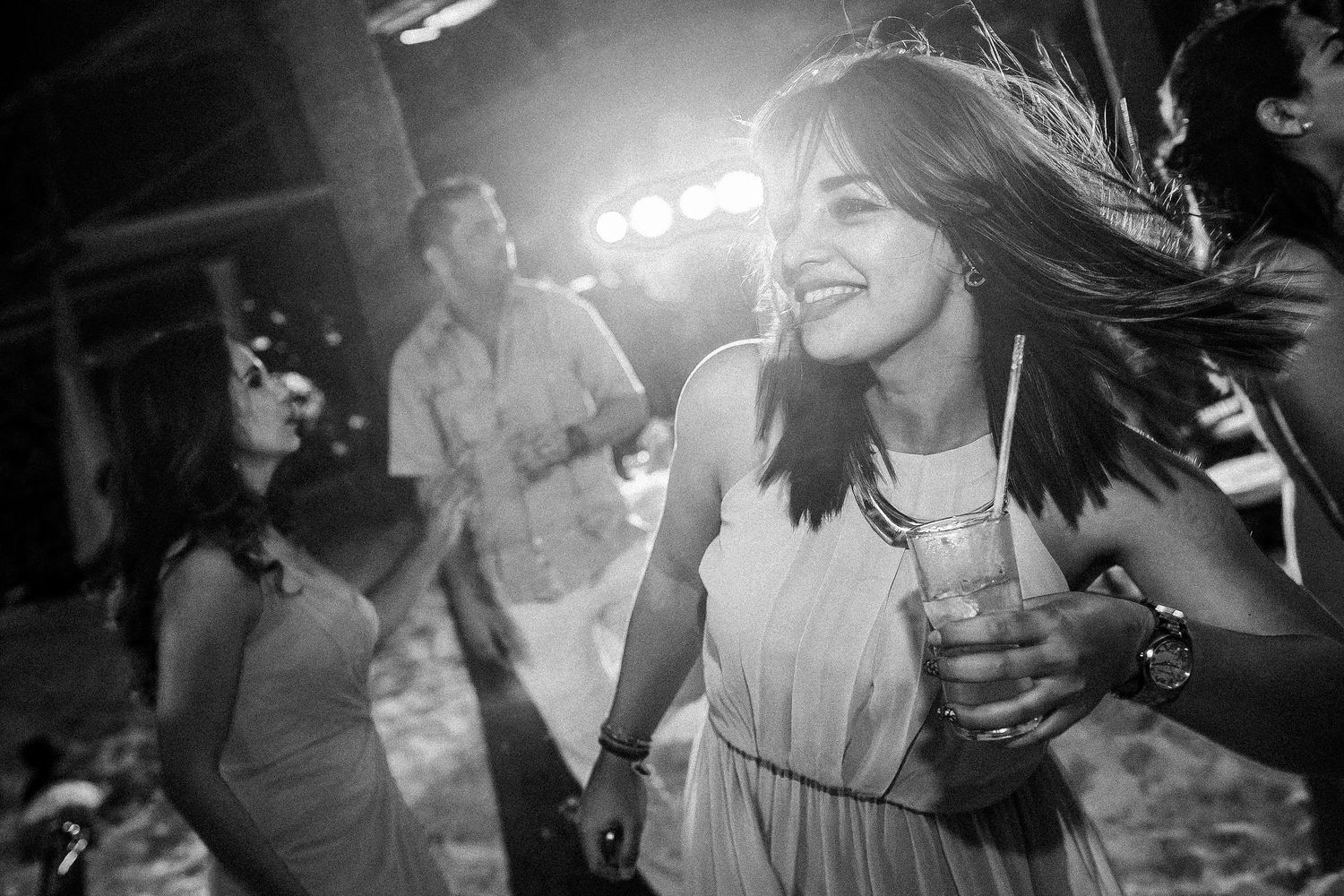 Black-and-white candid of a smiling guest holding a drink on the crowded wedding dance floor.