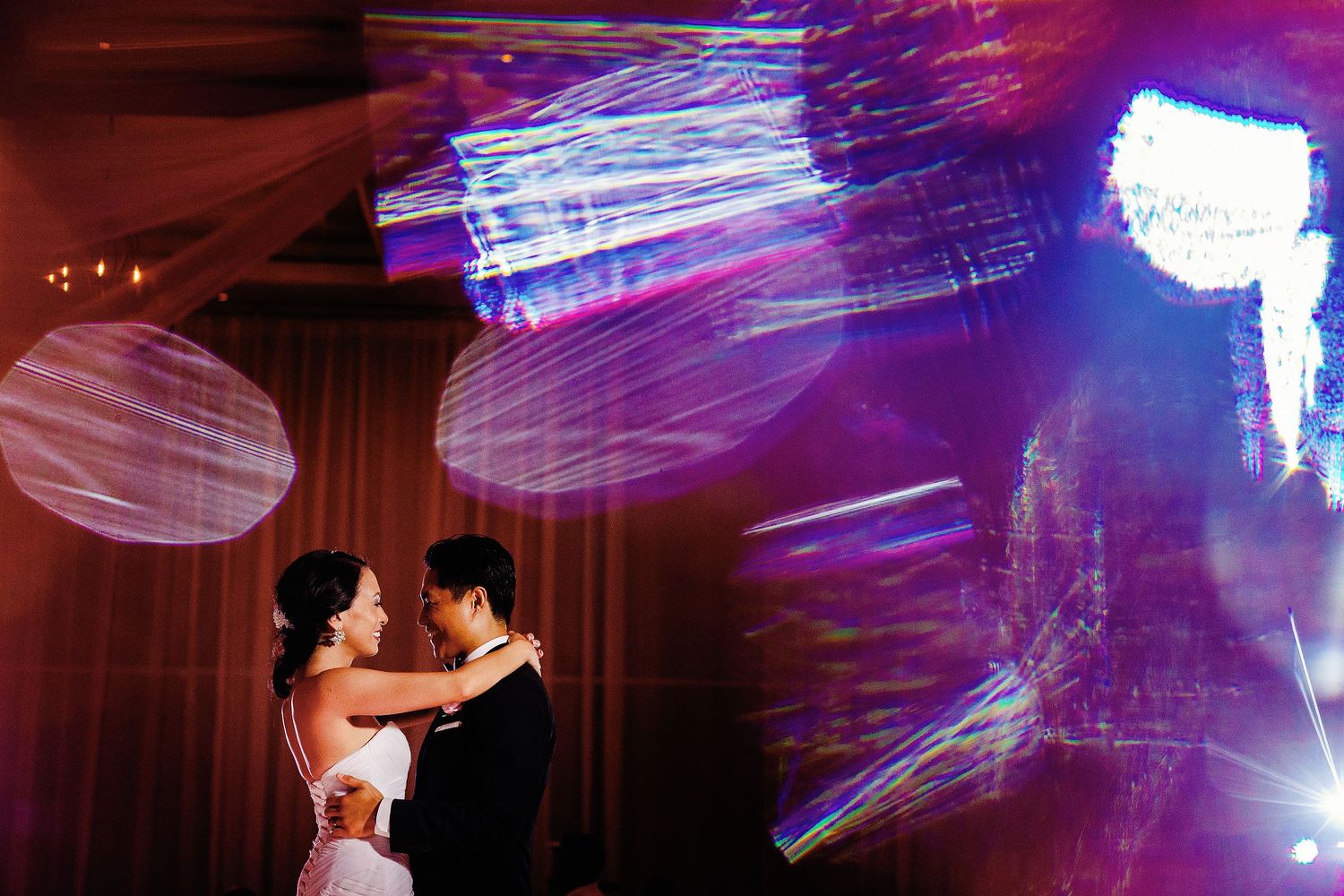 Newlyweds sharing their first dance during the wedding reception at Hard Rock Hotel Riviera Maya, surrounded by colorful artistic lighting.