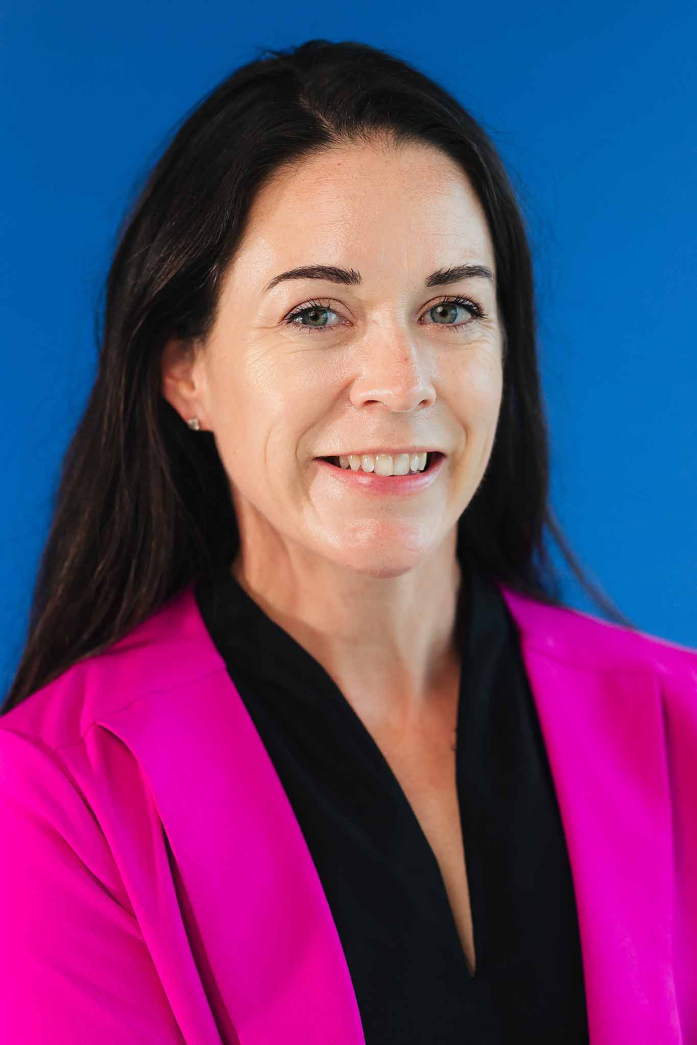 Professional corporate headshot photography Cancun with business portrait of woman wearing pink blazer on blue background