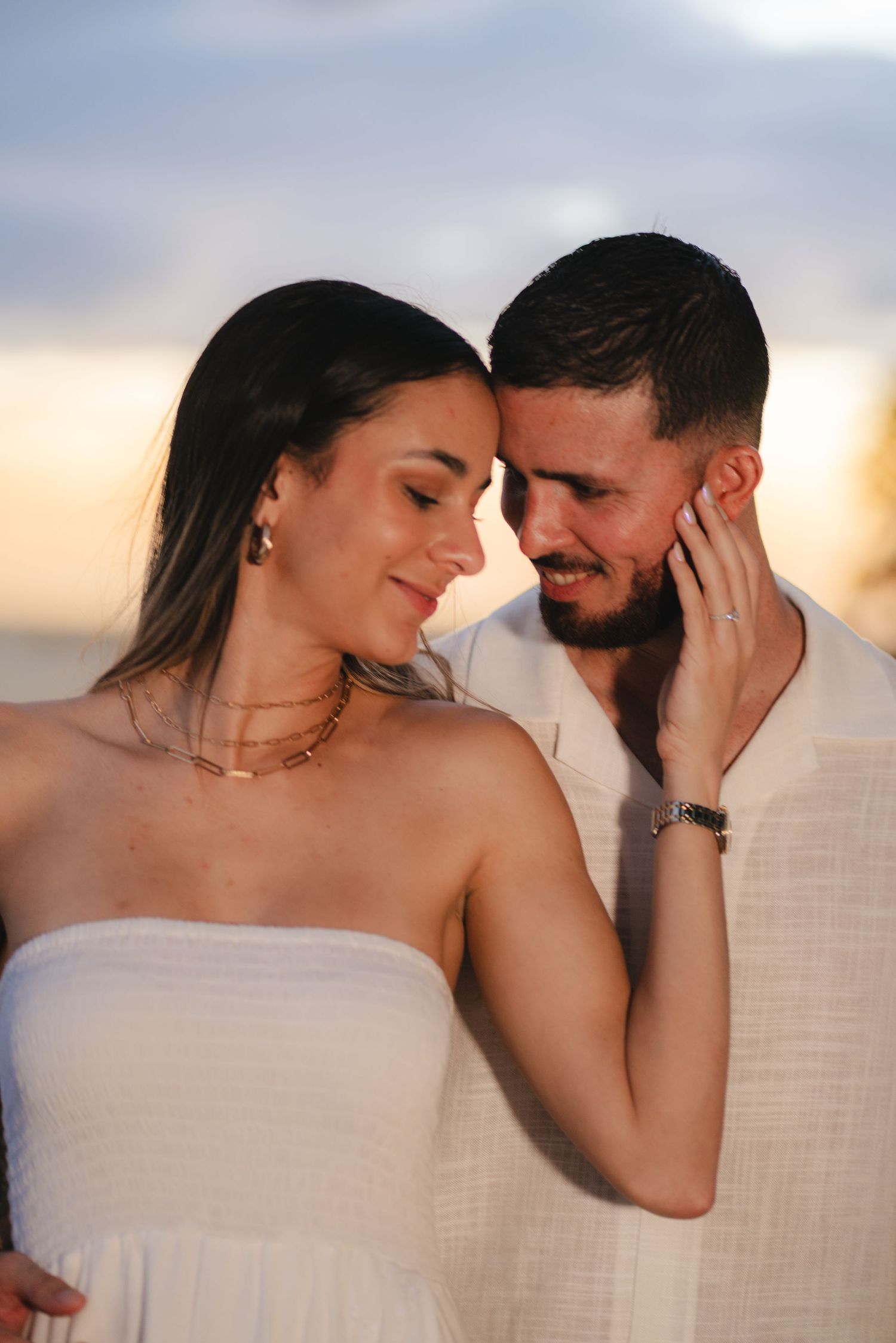 Romantic couple touching foreheads during a colorful beach sunset.