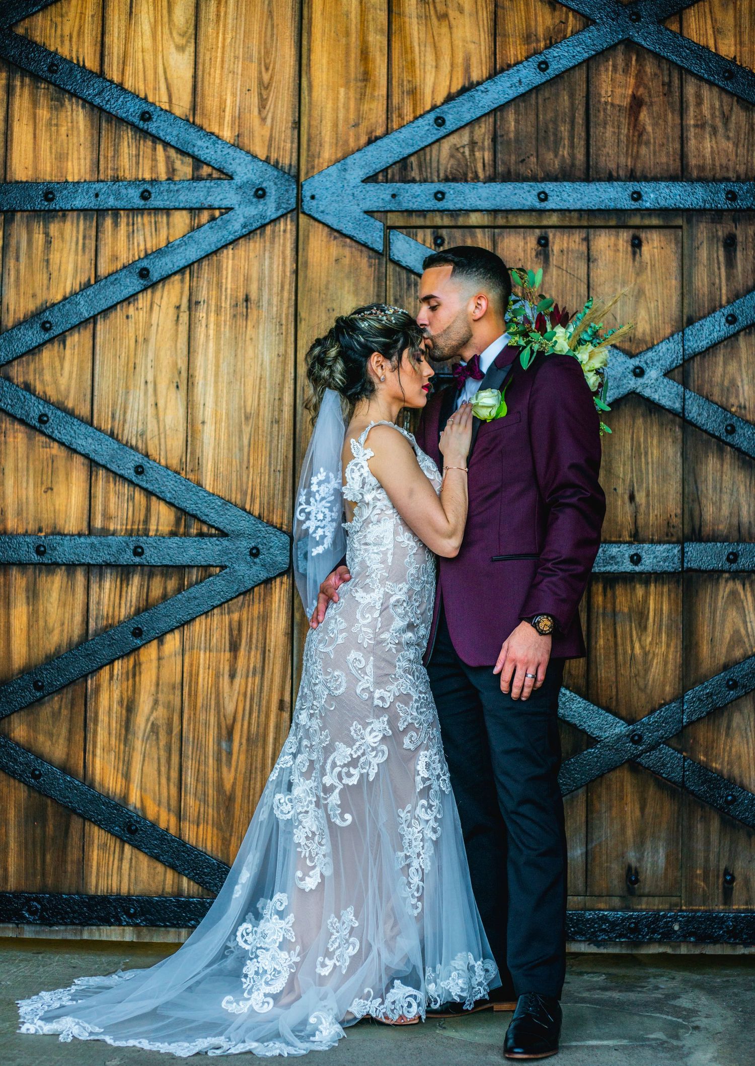 Wedding couple kissing in front of rustic wooden barn doors with iron details.