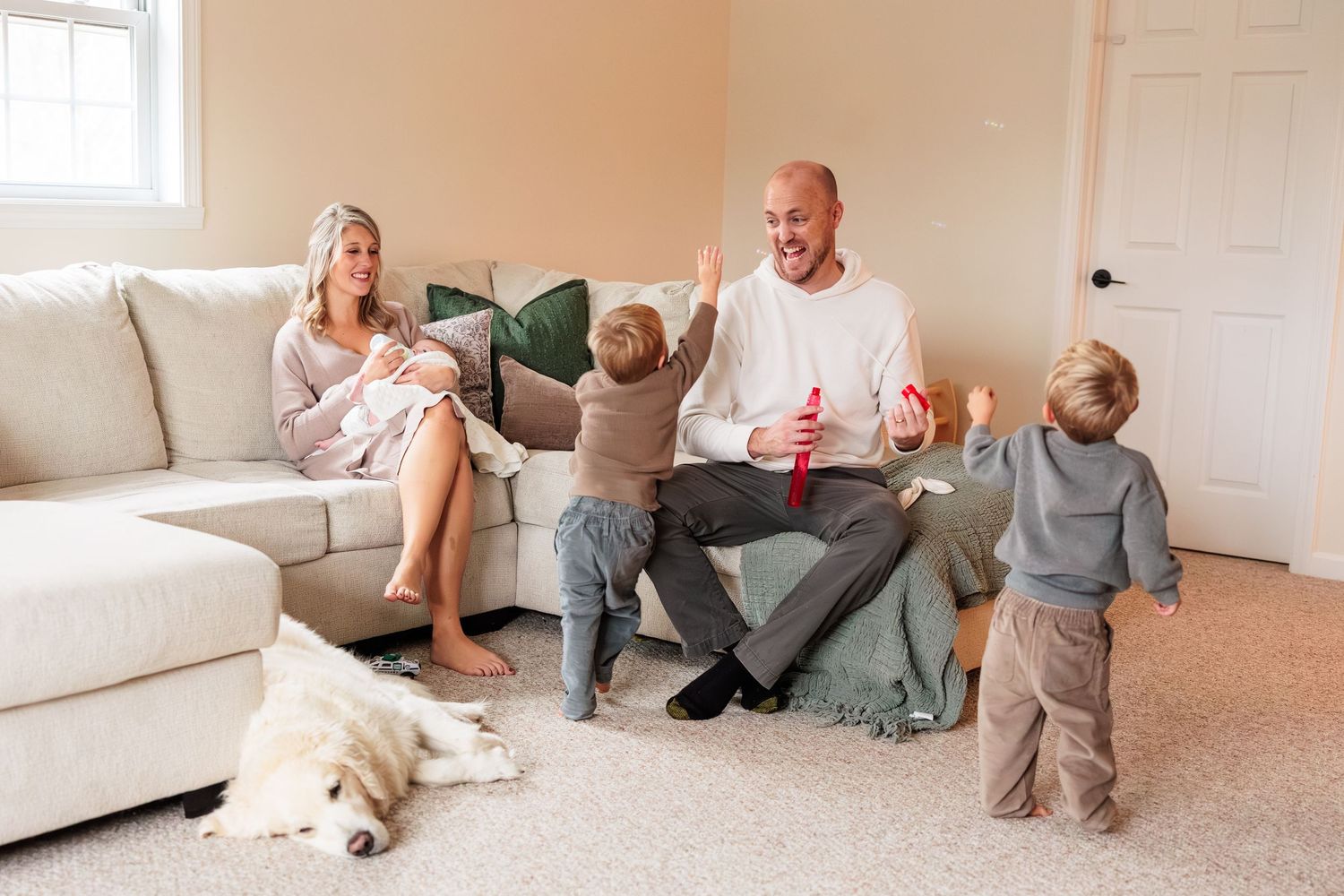 Family of five with golden retriever enjoying playful moment on living room floor with young children.