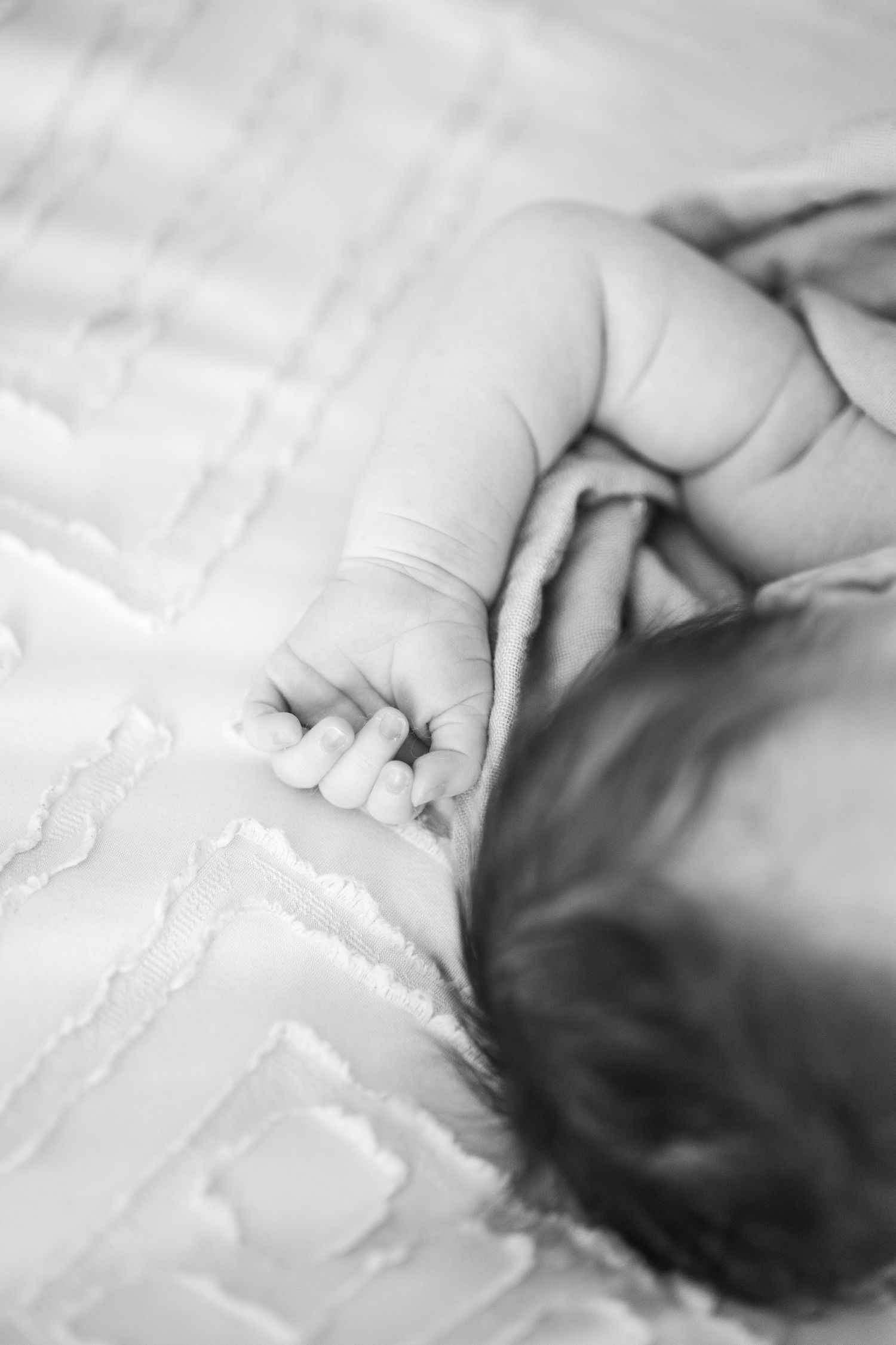 Close-up black and white photo of newborn baby tiny hand resting on quilted blanket.
