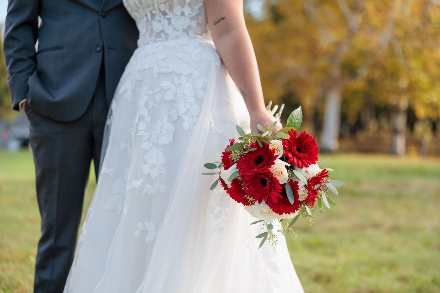Close-up of bride holding vibrant red and white wedding bouquet in lace gown.