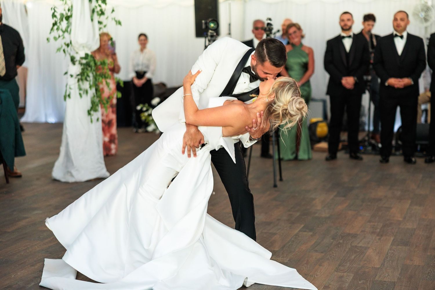 Groom dips bride in romantic first dance moment at elegant tented wedding reception.