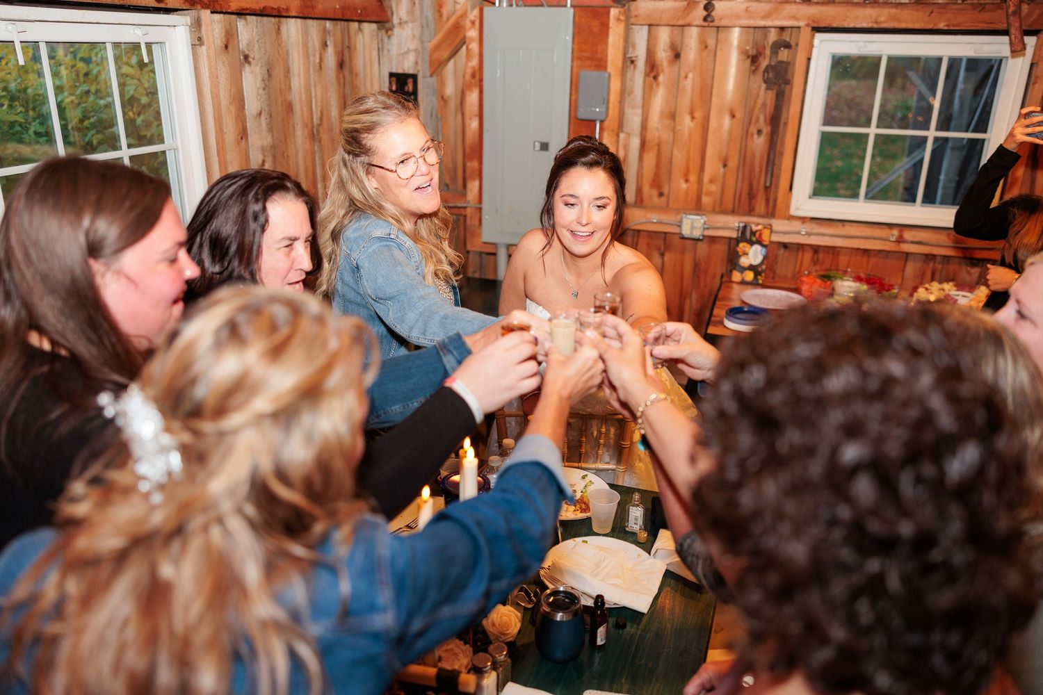 Bridesmaids and friends toast together with drinks in a cozy wooden cabin during wedding celebrations.