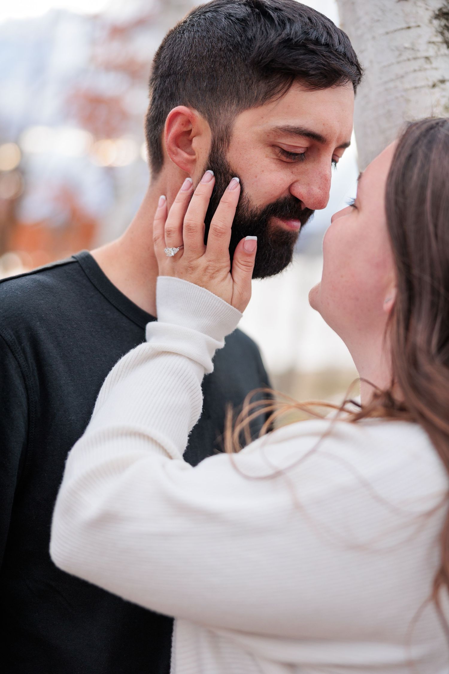 Close-up of woman tenderly holding mans bearded face as they share an intimate moment outdoors in fall.