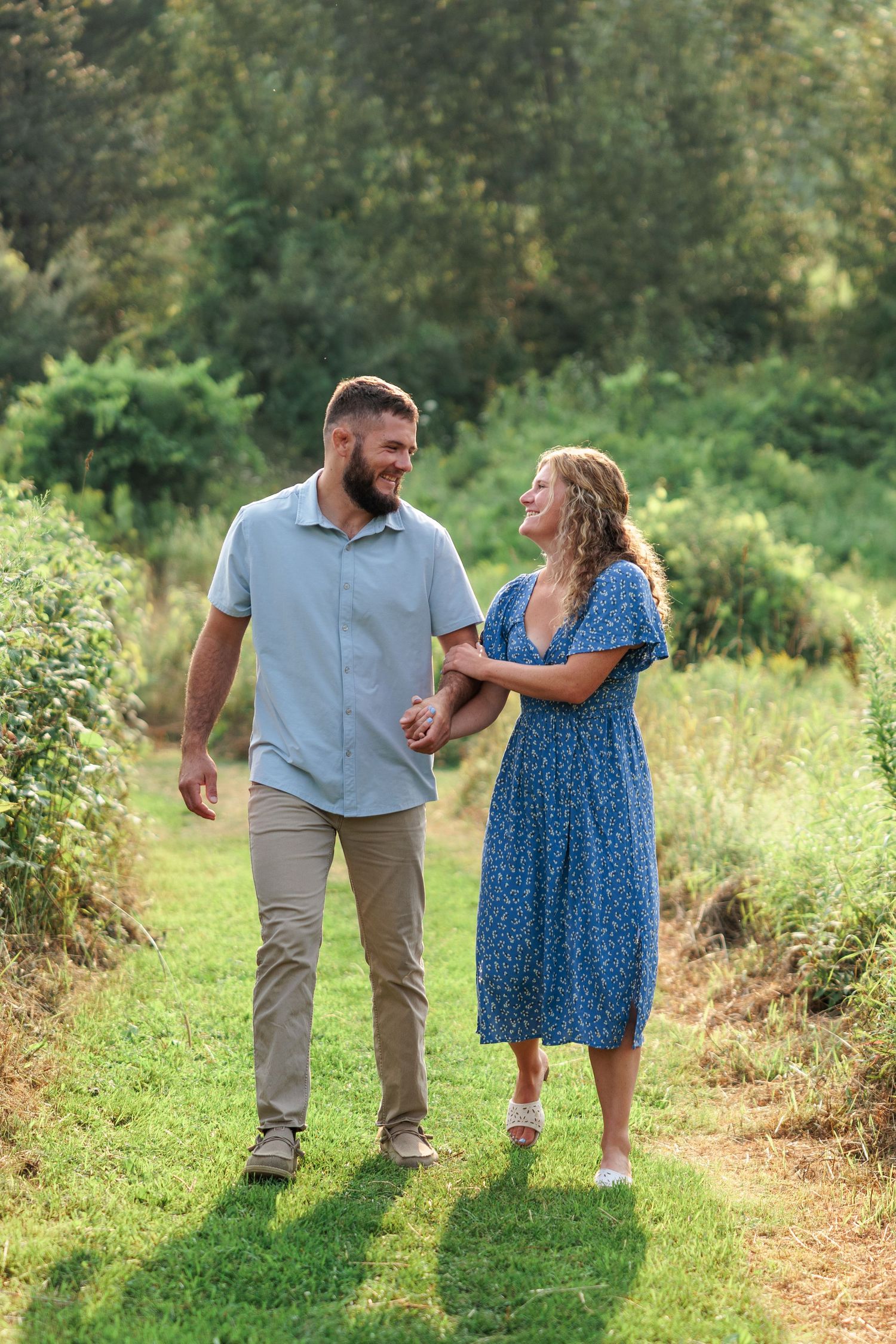 Smiling couple holding hands and walking along a lush green garden path on a sunny summer day.