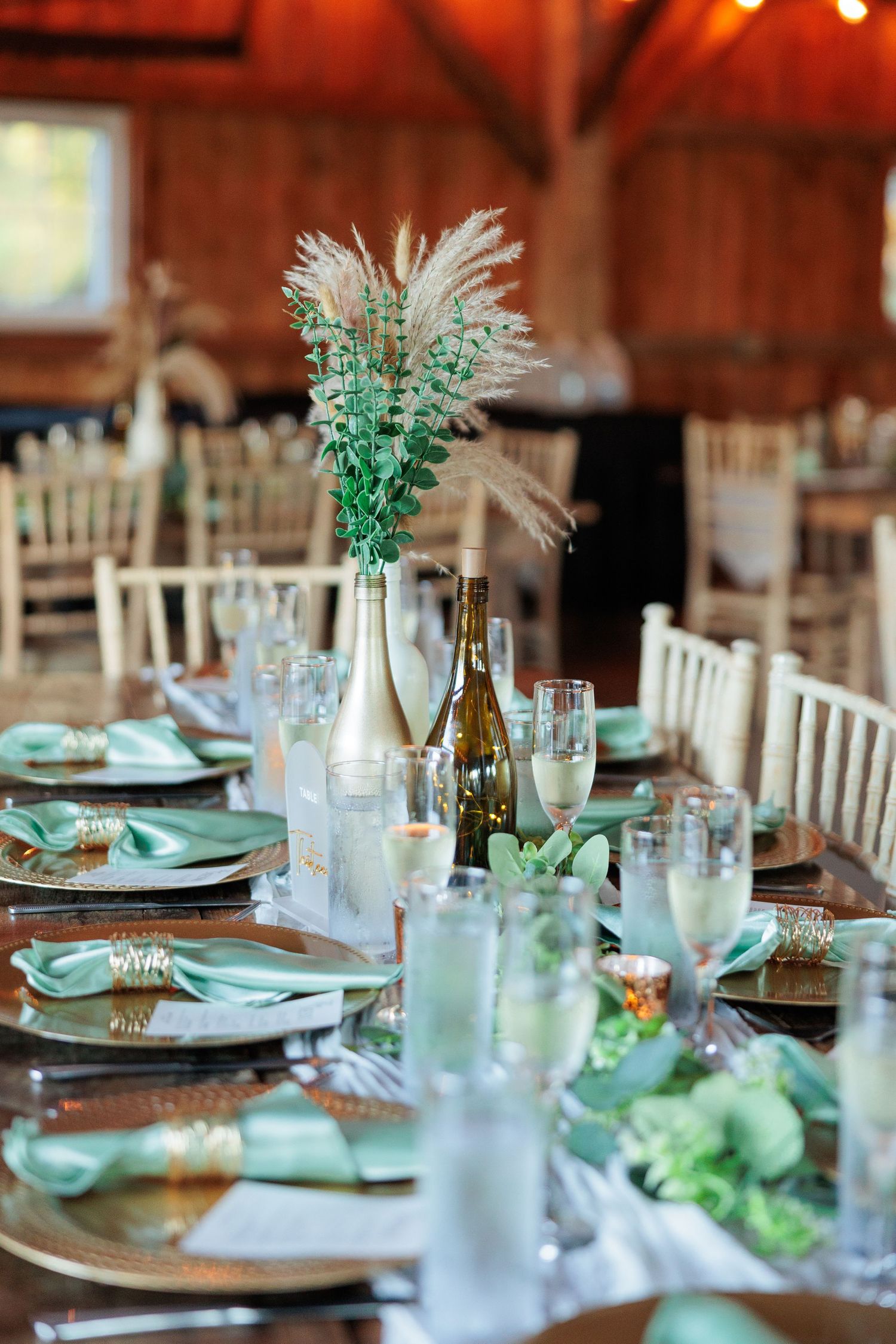 Elegant table settings with mint green accents and feather centerpieces in a rustic barn venue.