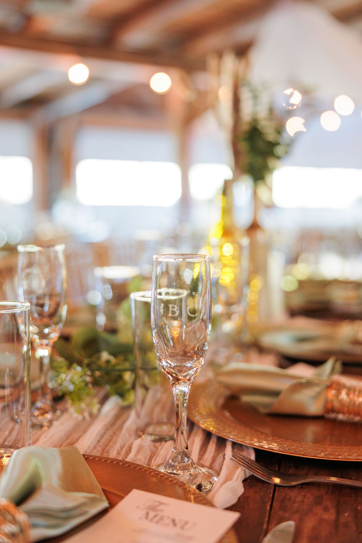 Wedding reception table settings with crystal glasses and blush napkins in natural light.