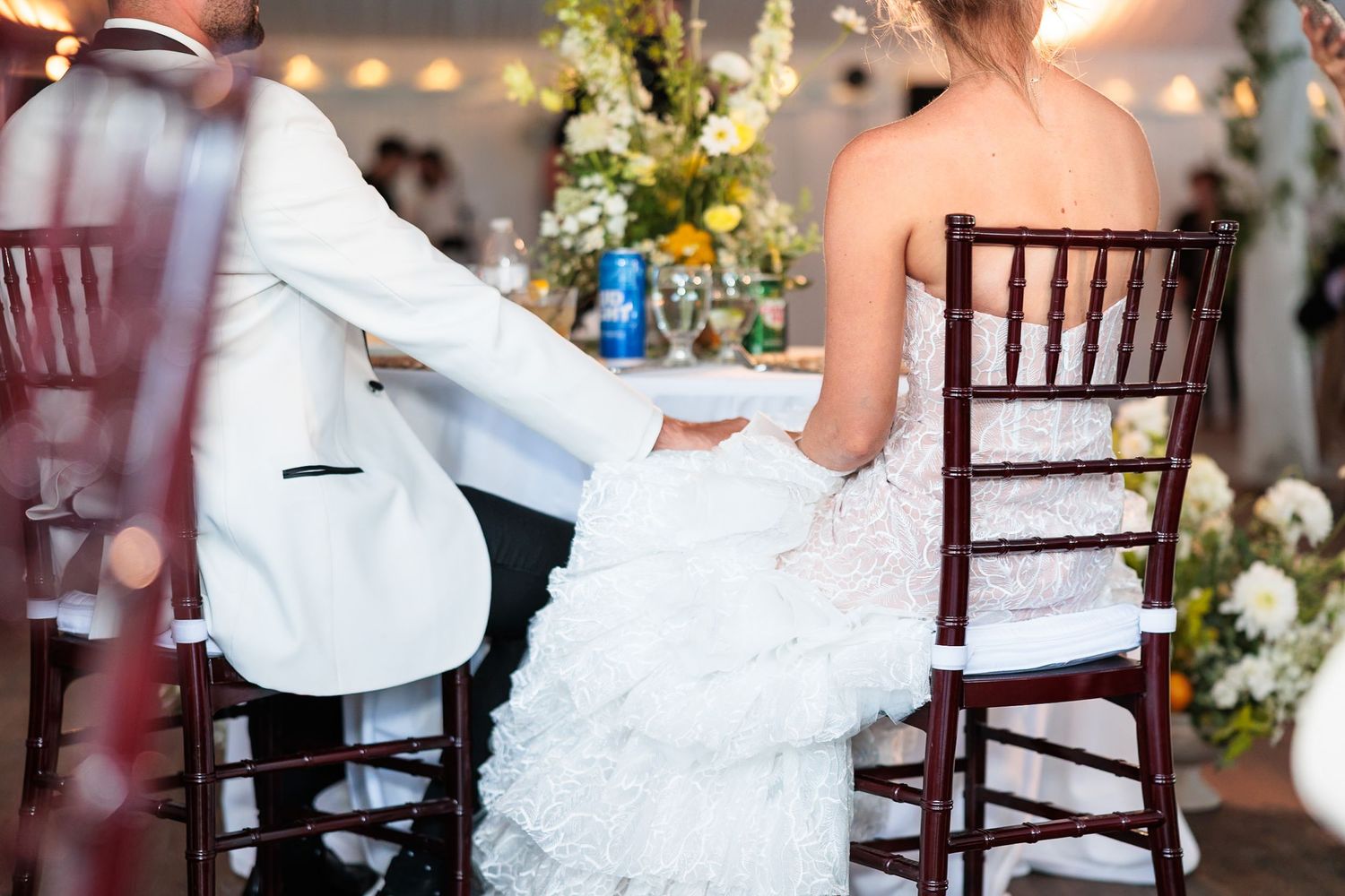 Bride and groom hold hands while seated at sweetheart table during wedding reception dinner.