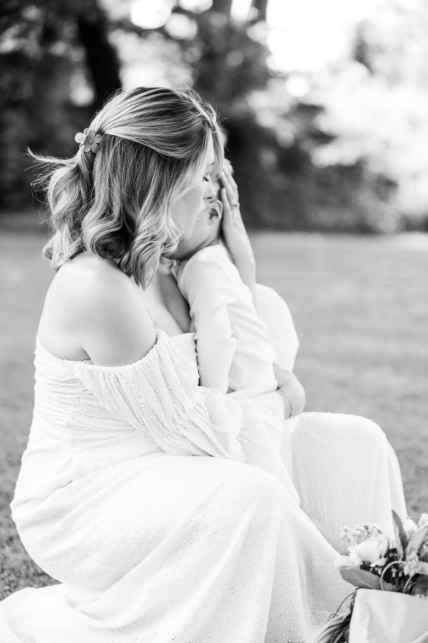 Black and white portrait of pregnant woman in off-shoulder dress sitting outdoors in garden.