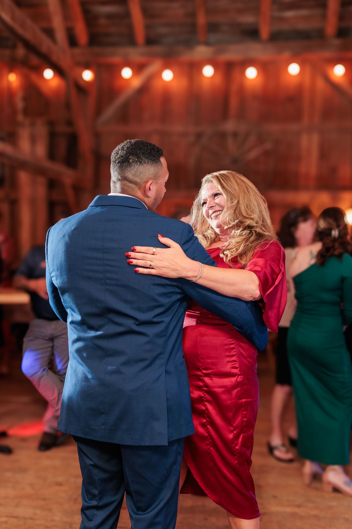 Couple dancing energetically in a rustic barn venue with string lights overhead.