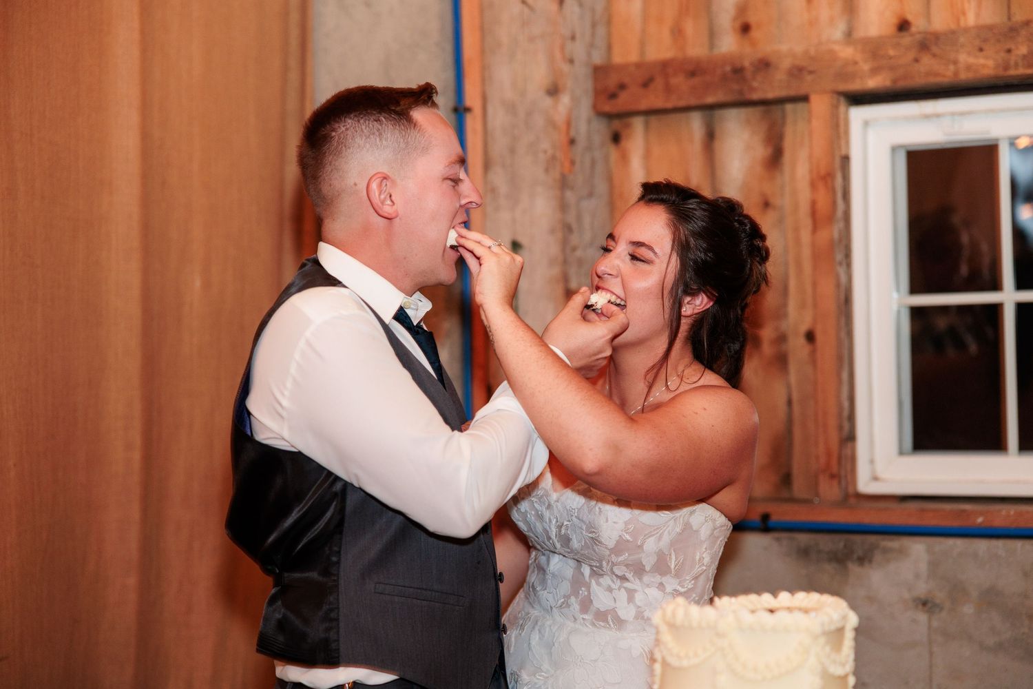 Smiling bride playfully smashes wedding cake into grooms face during fun reception cake cutting moment.