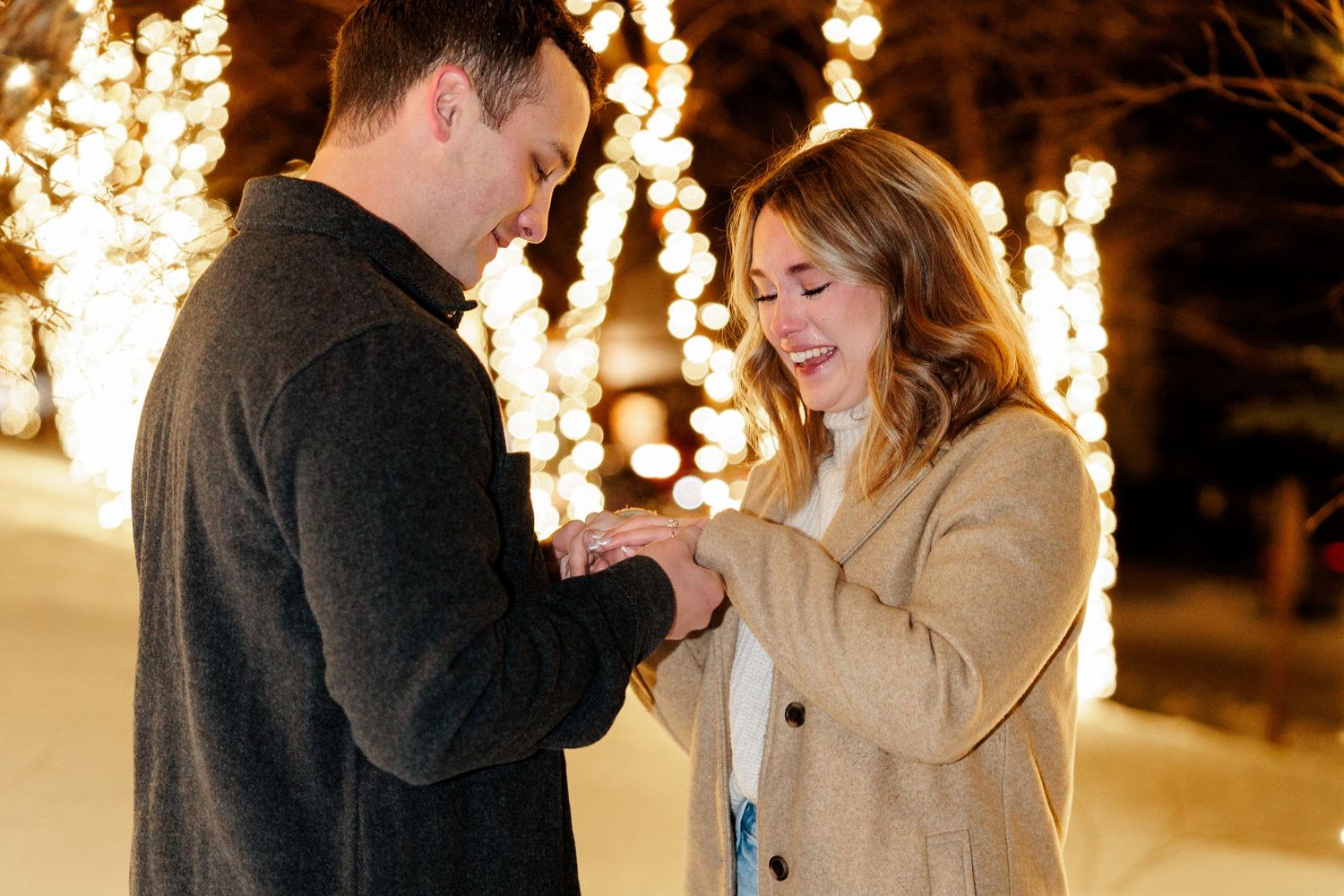 A couple shares a romantic moment during a winter evening proposal with glowing lights in the background.