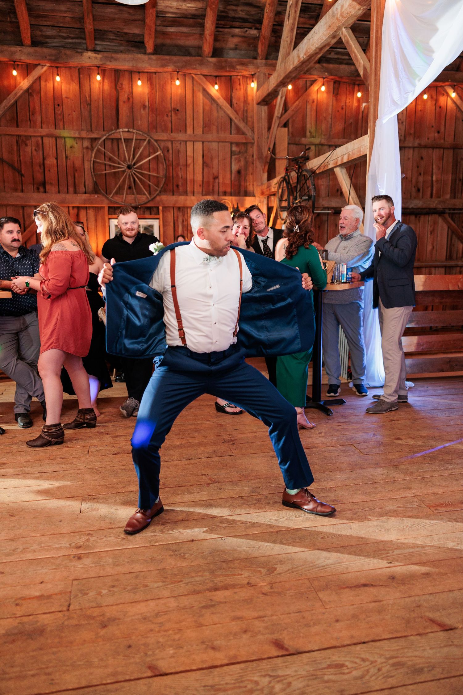 Wedding guests dancing and having fun on a wooden barn floor with string lights above.