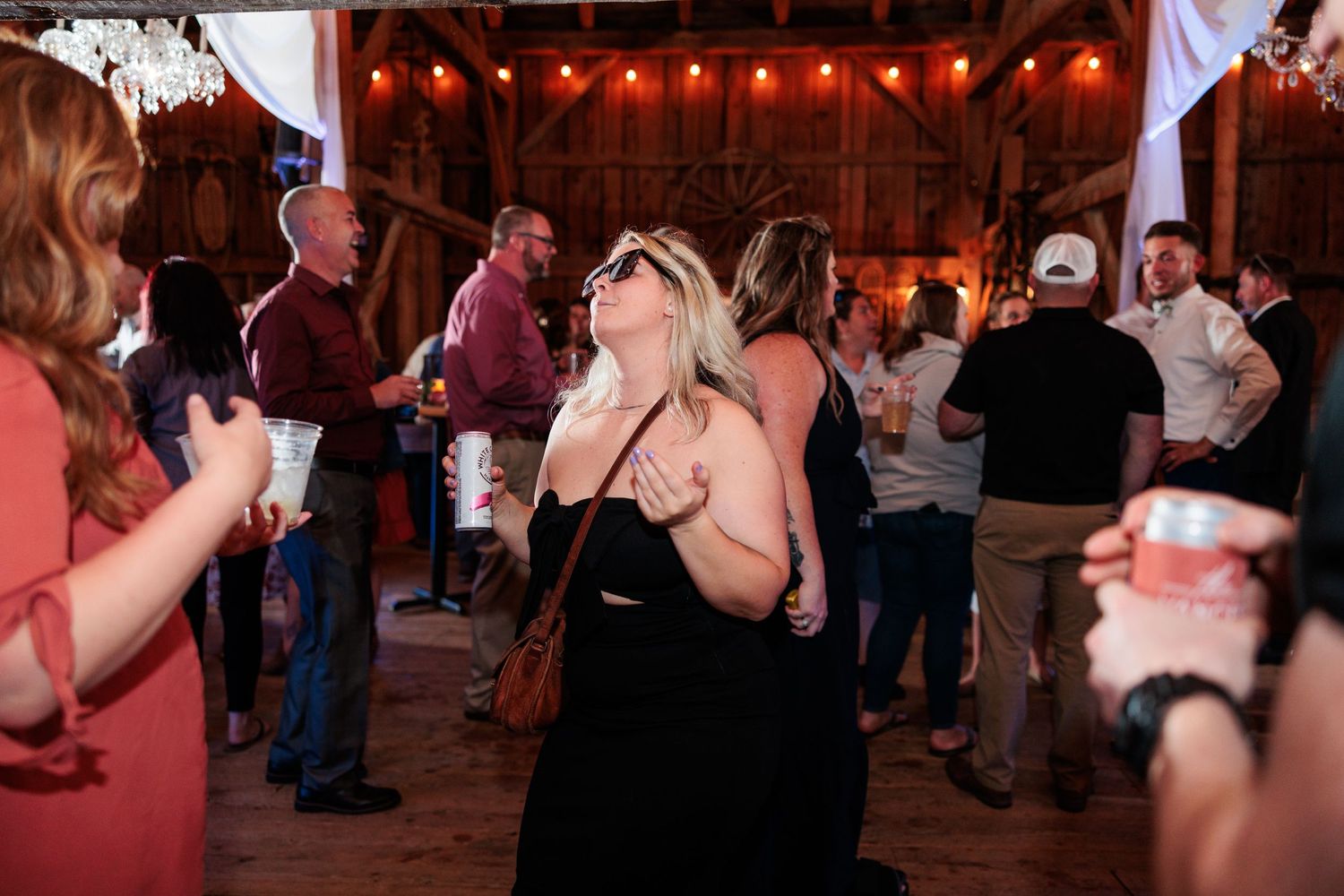 Wedding guests dance and celebrate on a rustic wooden dance floor under warm string lights.