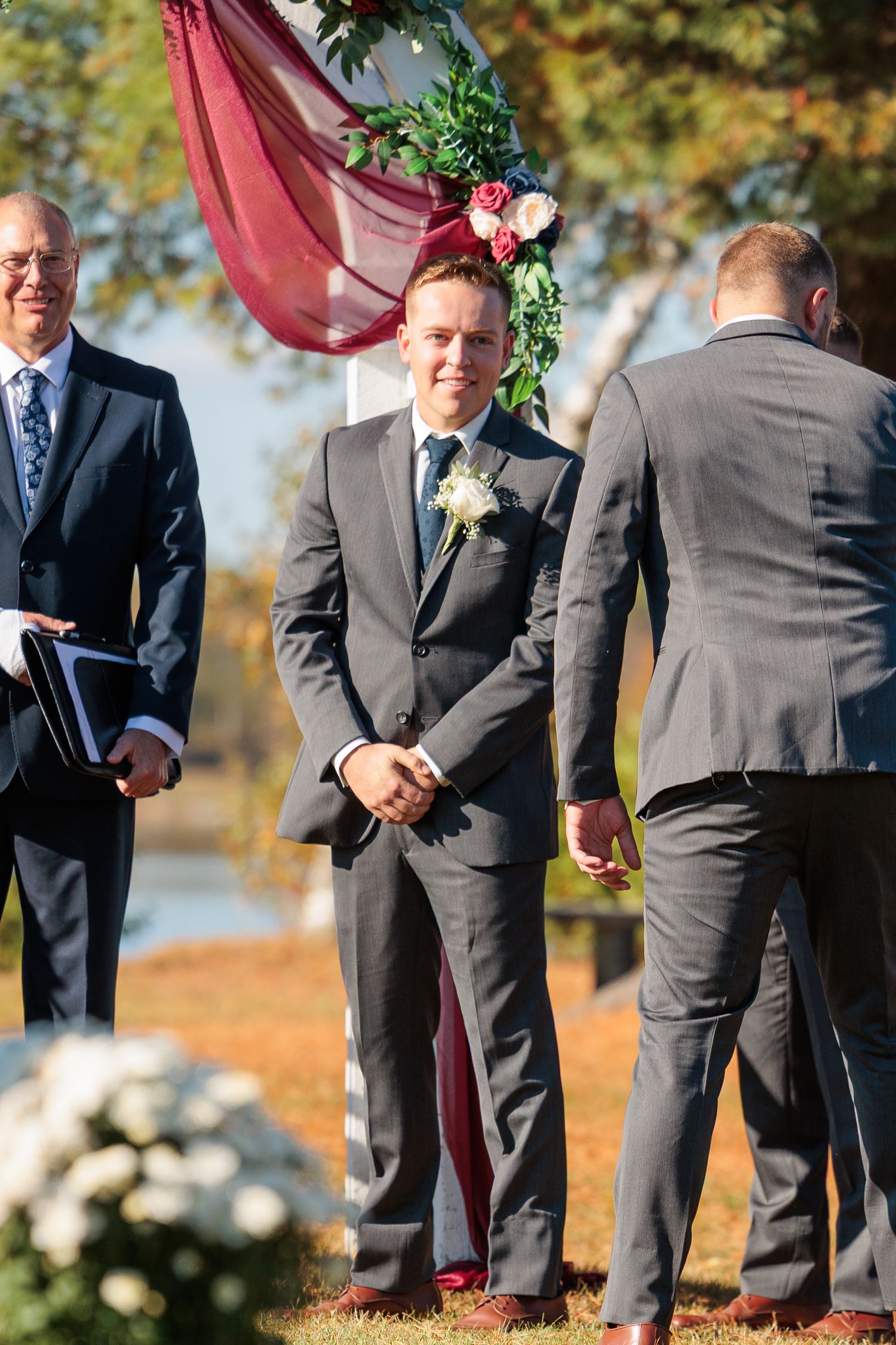 Groomsmen in dark suits stand together during an outdoor fall wedding ceremony.