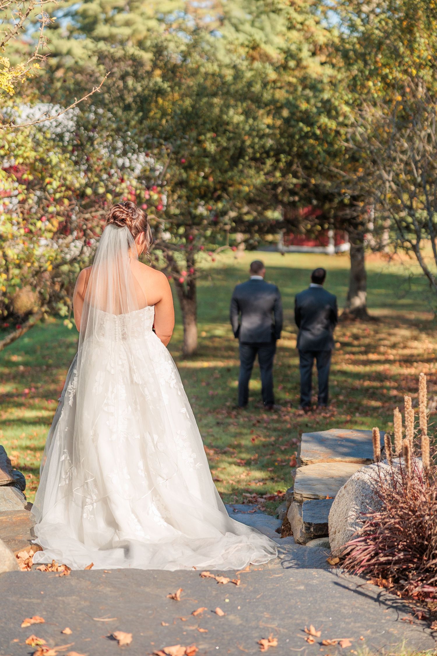 Wedding dress train trailing along autumn path with fallen leaves and trees.