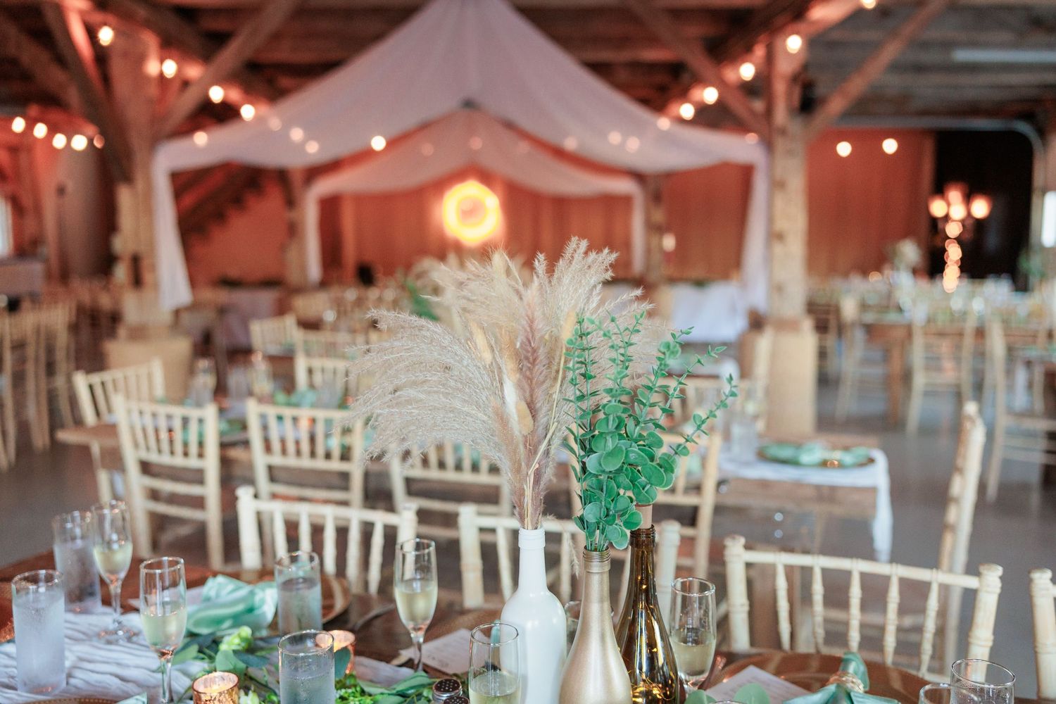 Long reception tables set with white chairs and mint green decor in a barn setting.