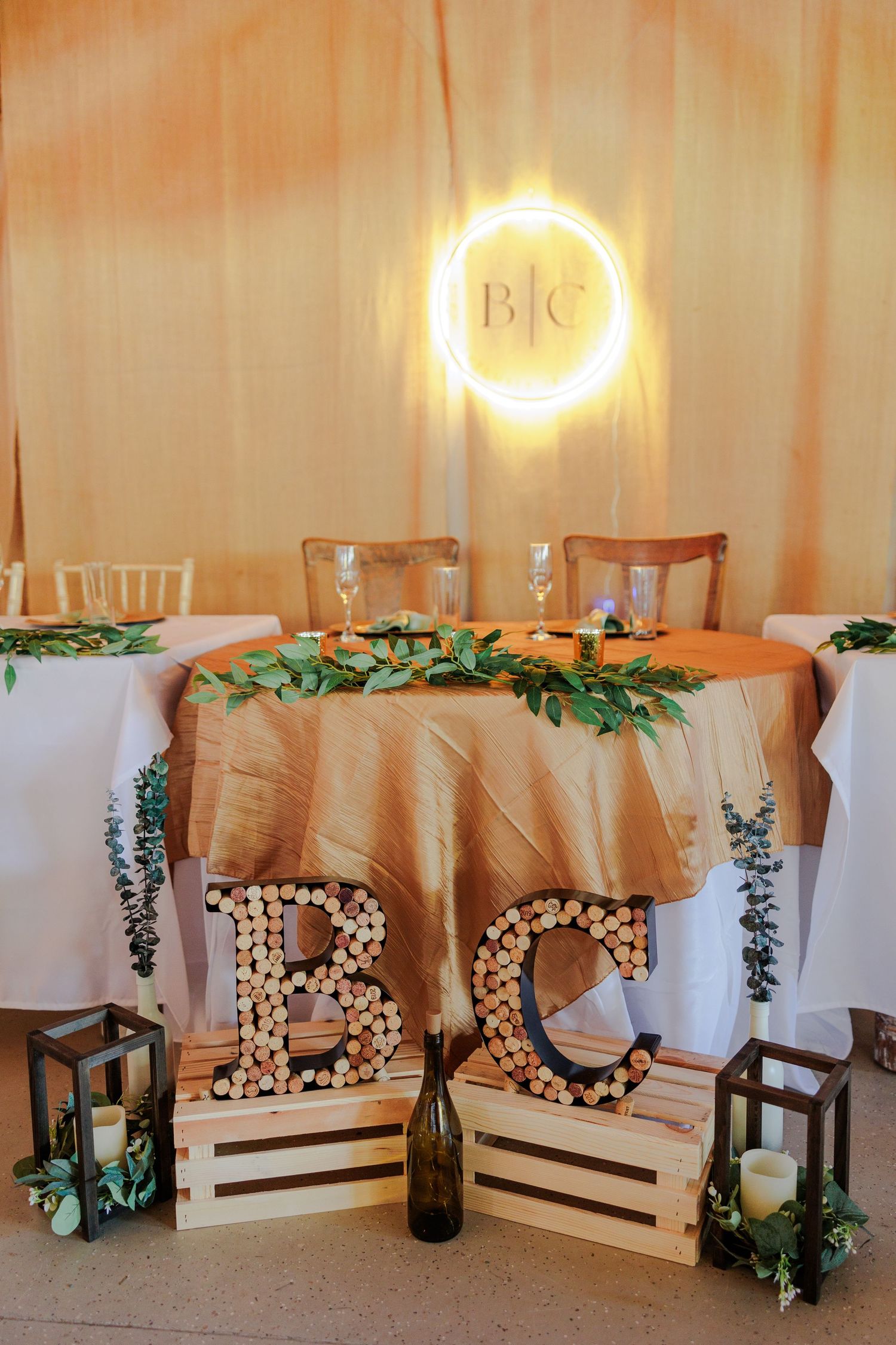 Illuminated wedding decor with floral letters and greenery against a draped backdrop.