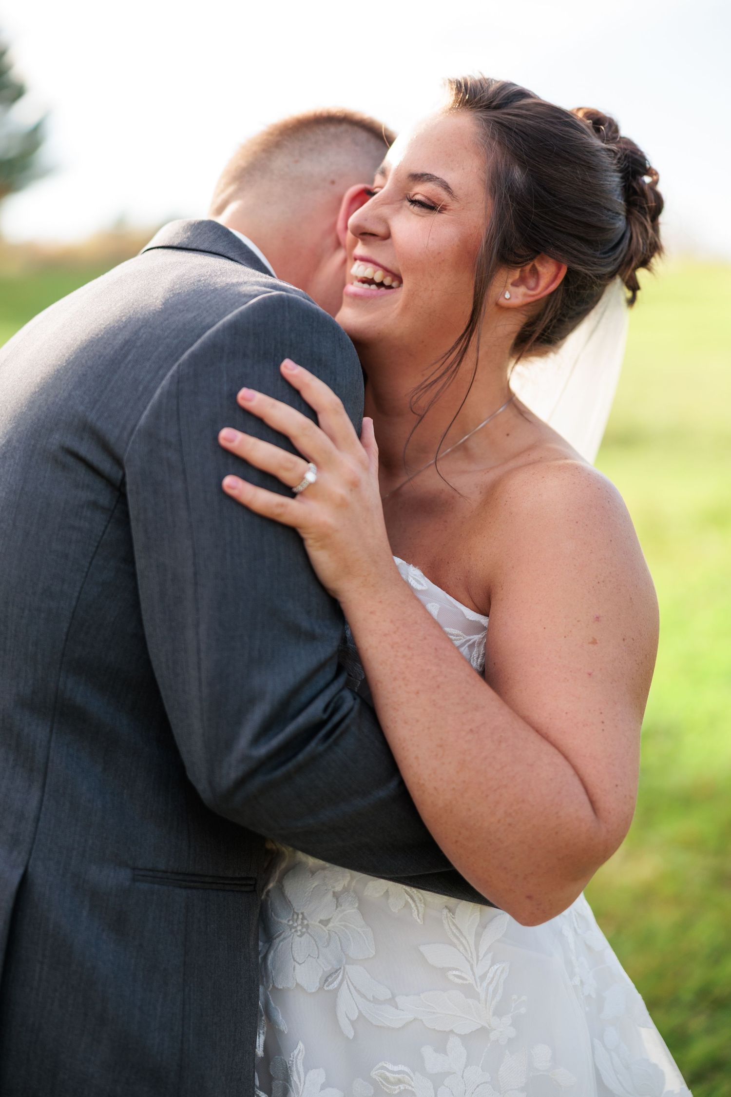 Laughing bride embracing groom outdoors in a joyful wedding portrait on green grass.