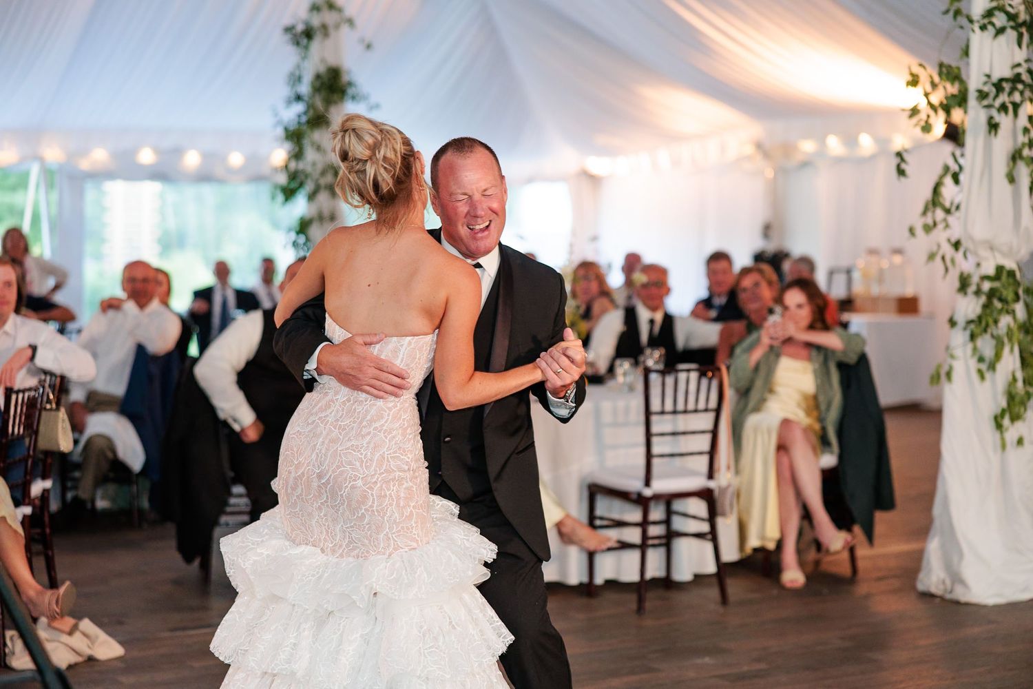 Bride in ruffled gown shares emotional father-daughter dance at elegant tented wedding reception.