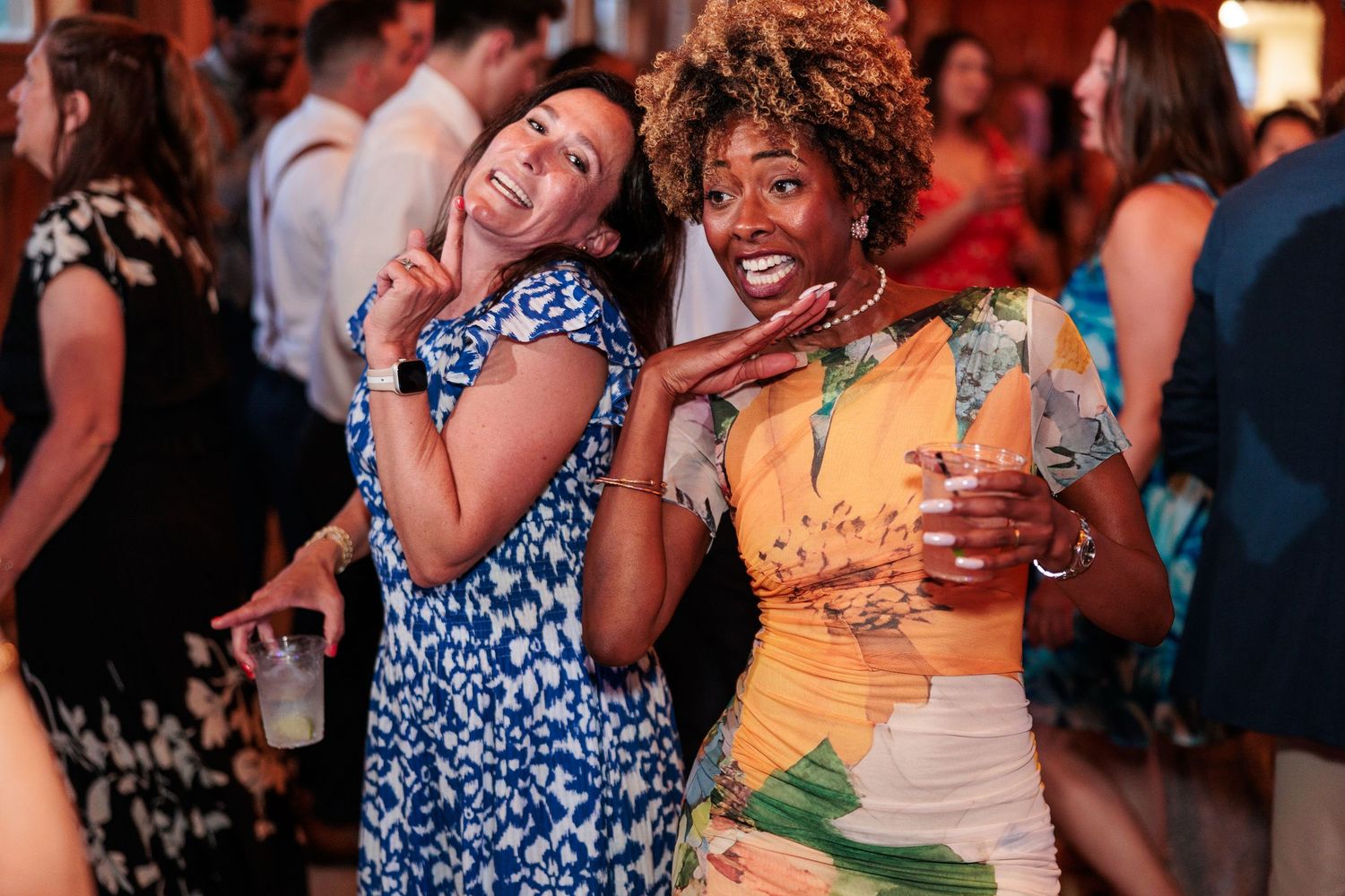 Two joyful women in colorful dresses pose and smile together while celebrating at a wedding reception.