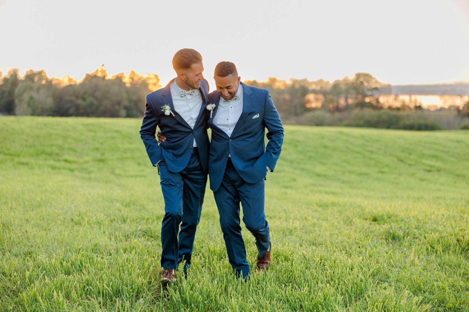 Wedding party members walk across green field during sunset photo session.