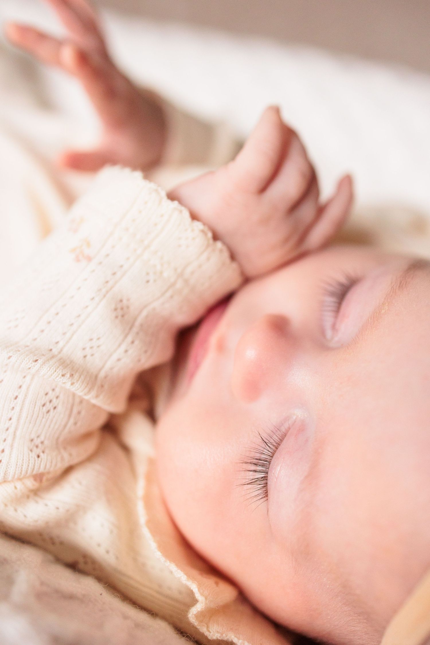 Closeup of sleeping baby in cream knit outfit showing peaceful expression and long eyelashes.