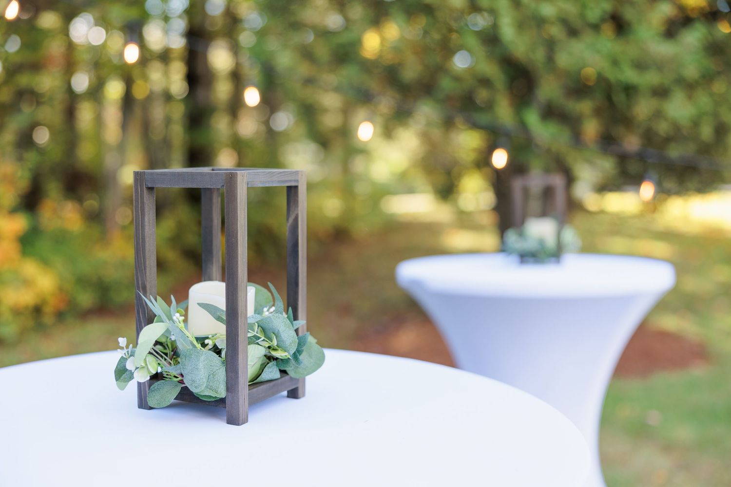 Outdoor wedding decor with white linens and wooden accents in natural sunlight.