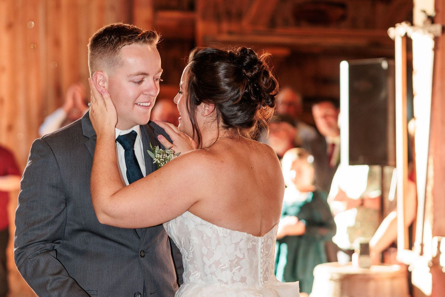 A couple shares their first dance in a rustic barn setting with warm lighting.