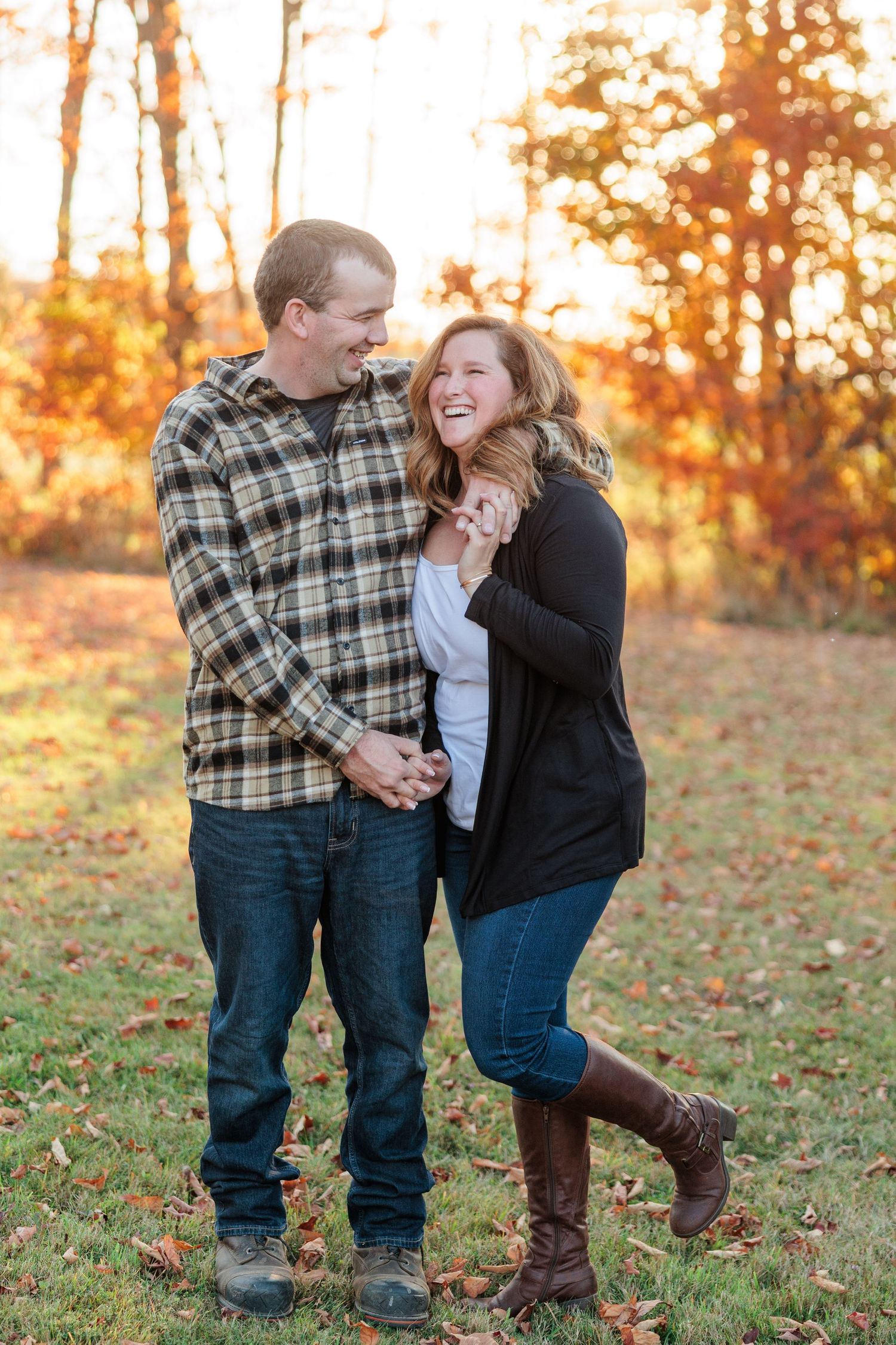 Happy couple laughing together in a sunlit autumn field surrounded by colorful fall foliage.
