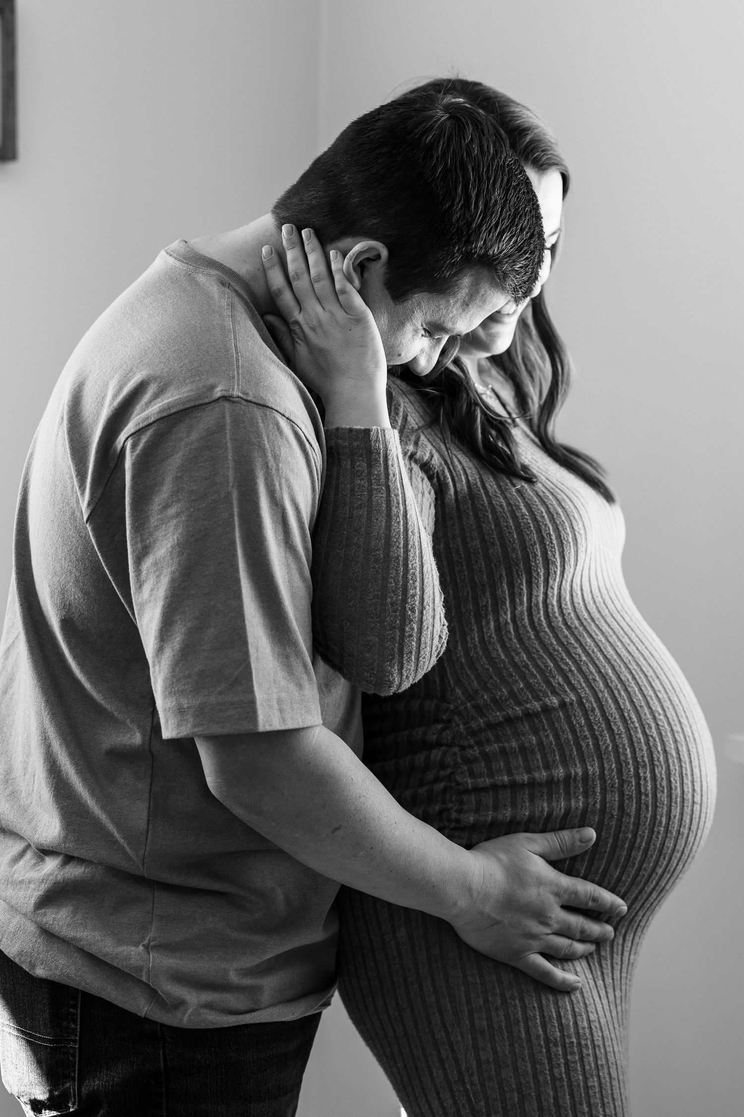 Black and white photo of a couple tenderly embracing, with the man holding a pregnant woman's baby bump.