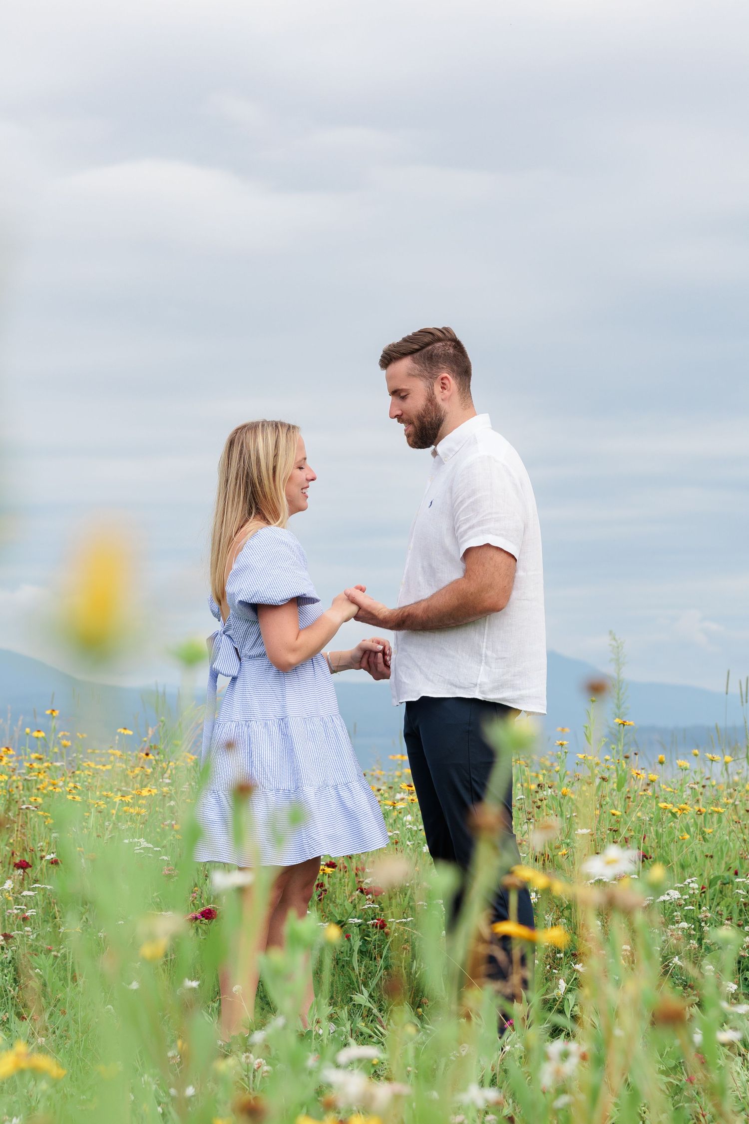 Couple standing face to face holding hands in a vibrant wildflower field under a cloudy sky.