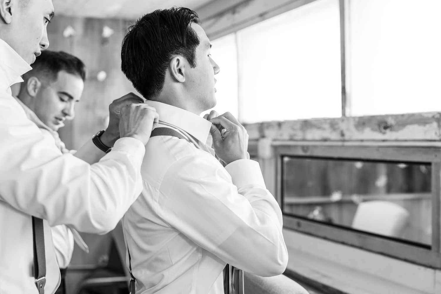 Black and white photo of groomsmen helping groom adjust tie before wedding ceremony.